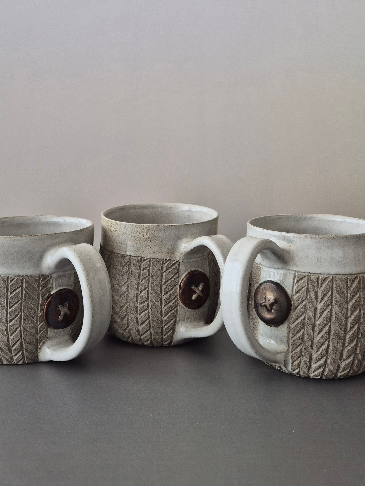 Three gray ceramic mugs with textured design and button detail on a gray surface.