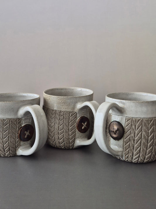 Three gray ceramic mugs with textured design and button detail on a gray surface.