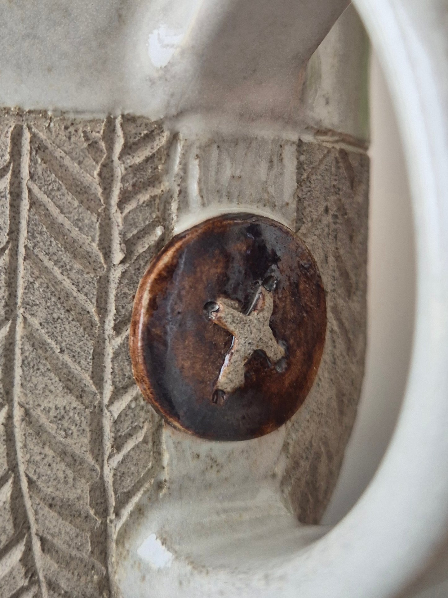 Close-up of a ceramic mug with a decorative button featuring a cross design.