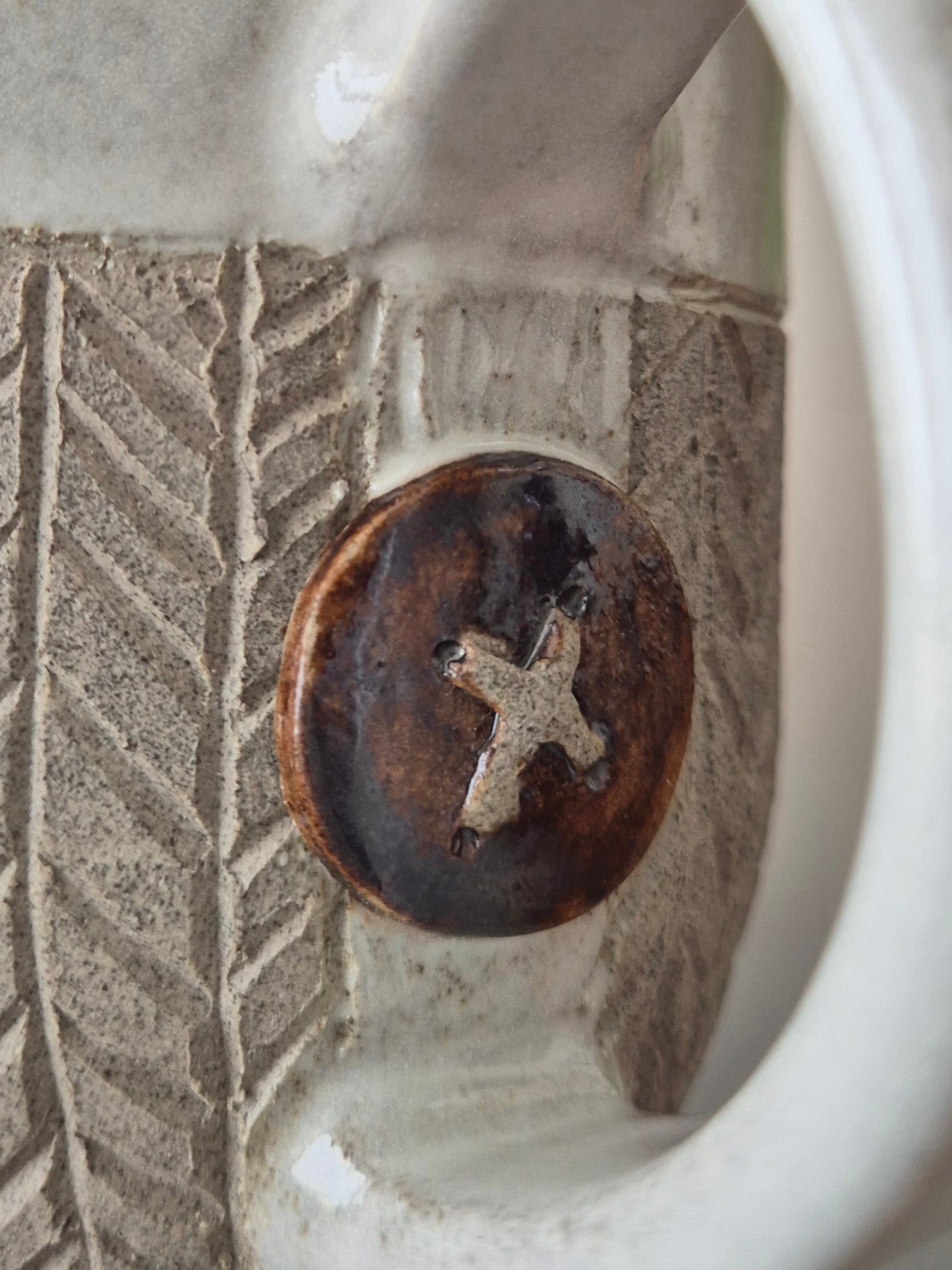 Close-up of a ceramic mug with a decorative button featuring a cross design.