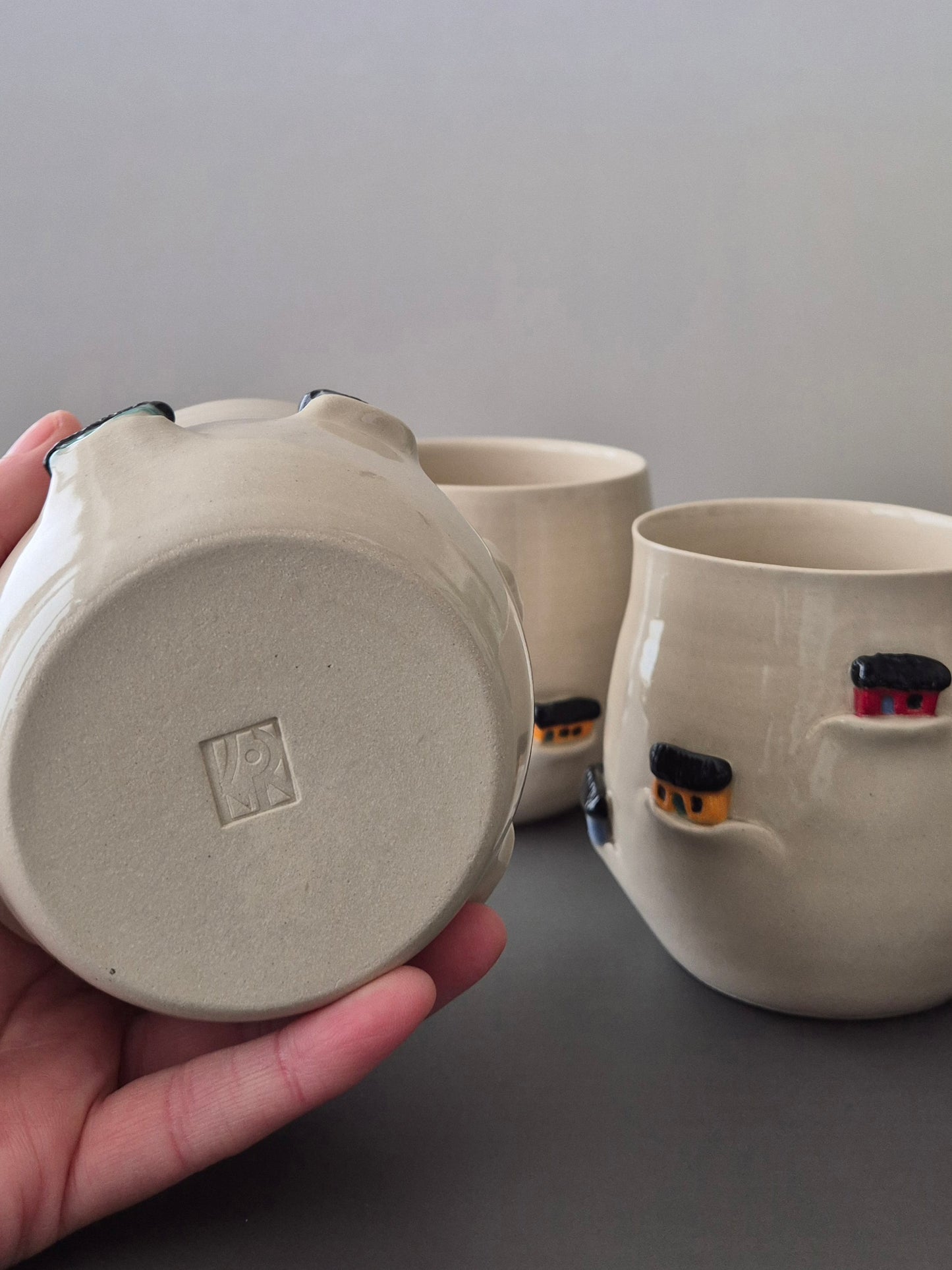 Ceramic mug with small decorative elements held by a hand against a neutral background