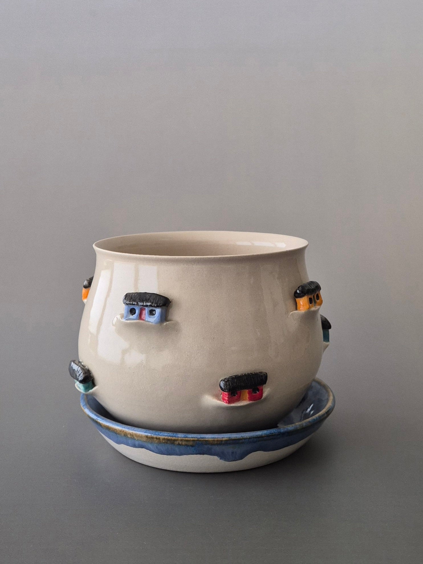 Ceramic plant pot with colourful tiny houses around the outer edge on a gray background