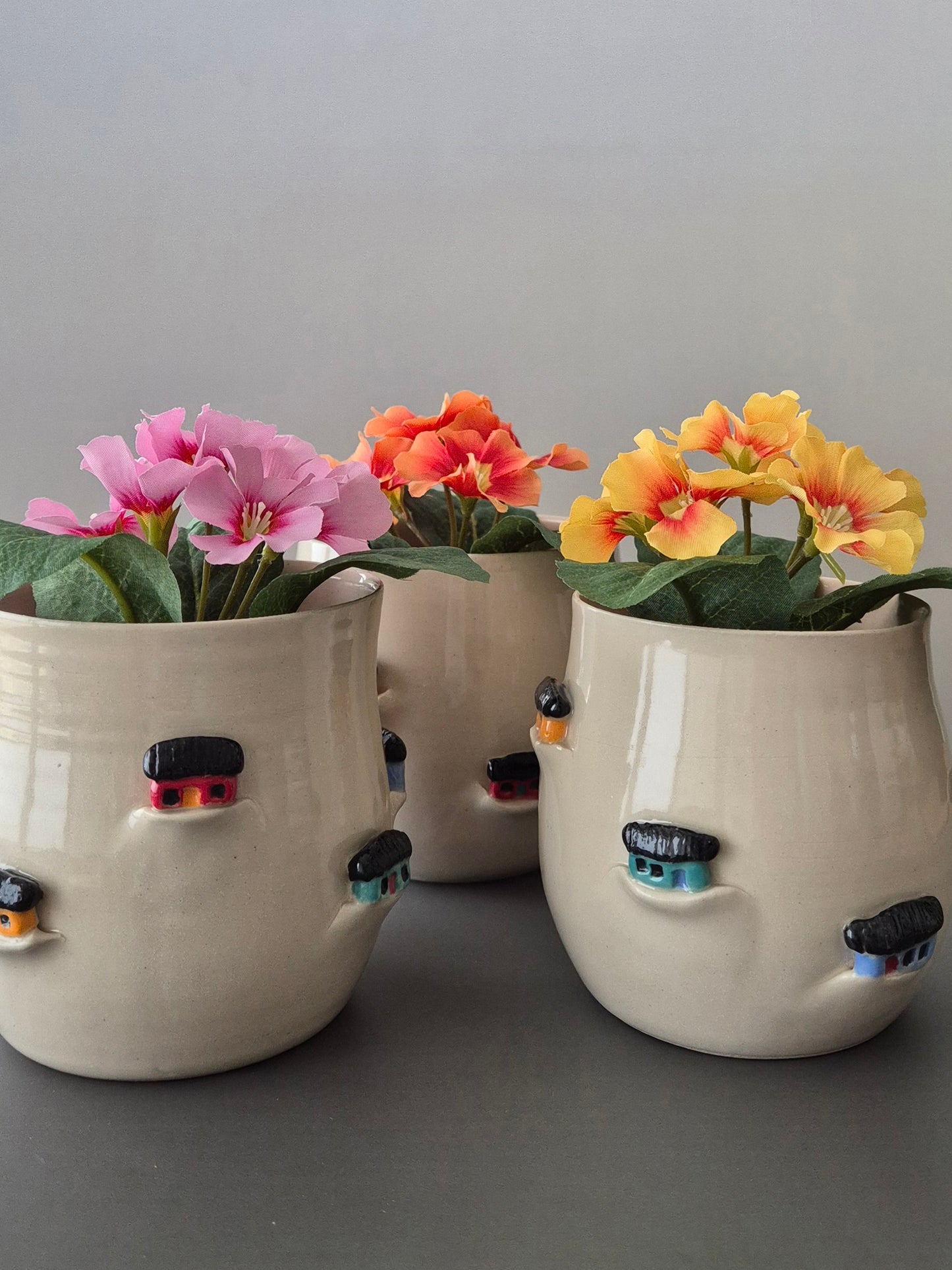 Three ceramic planters with tiny sculptural houses on a gray background