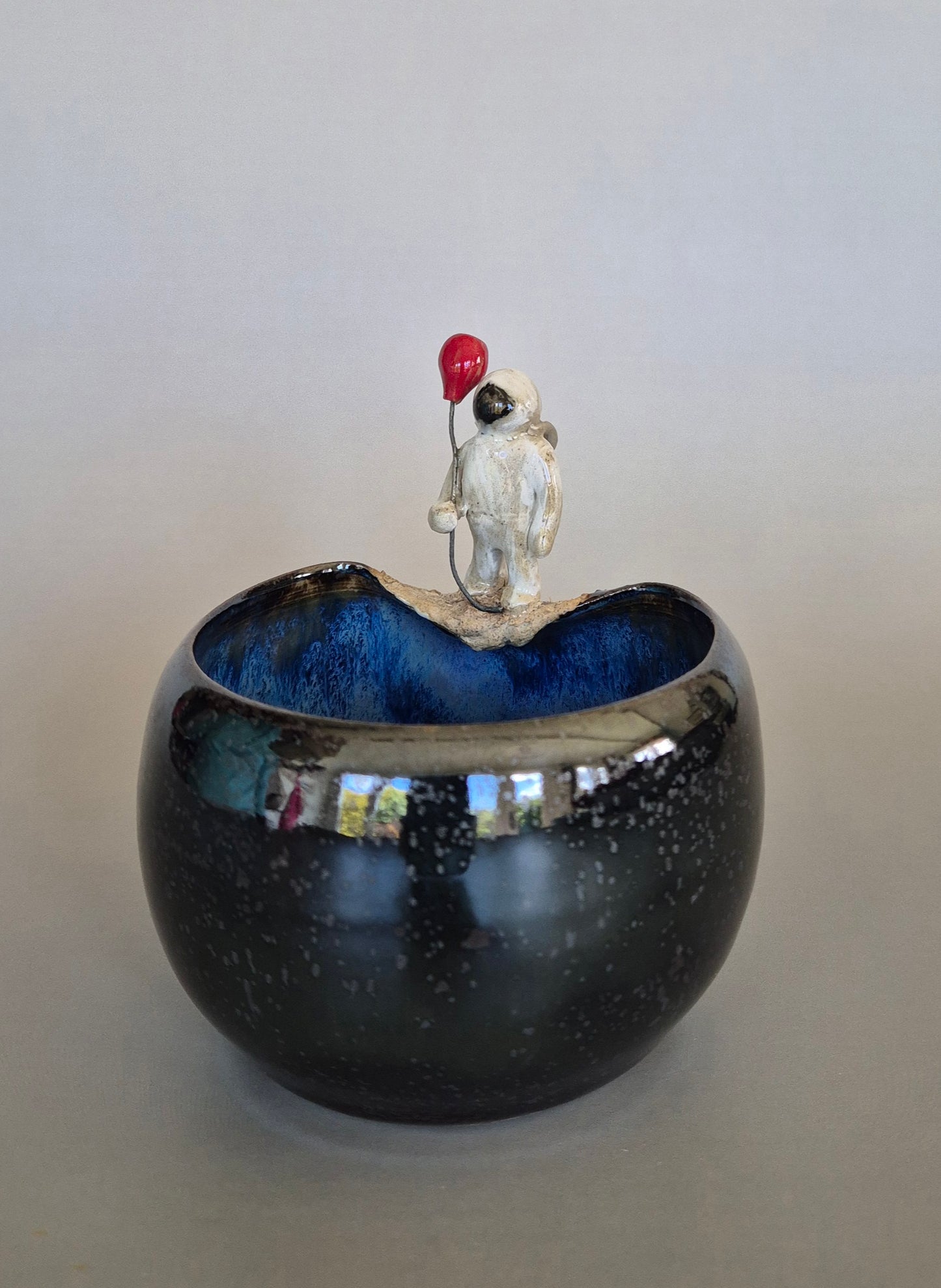 Ceramic bowl with a small sculptured figurine of an astronaut holding a red balloon. On a plain background