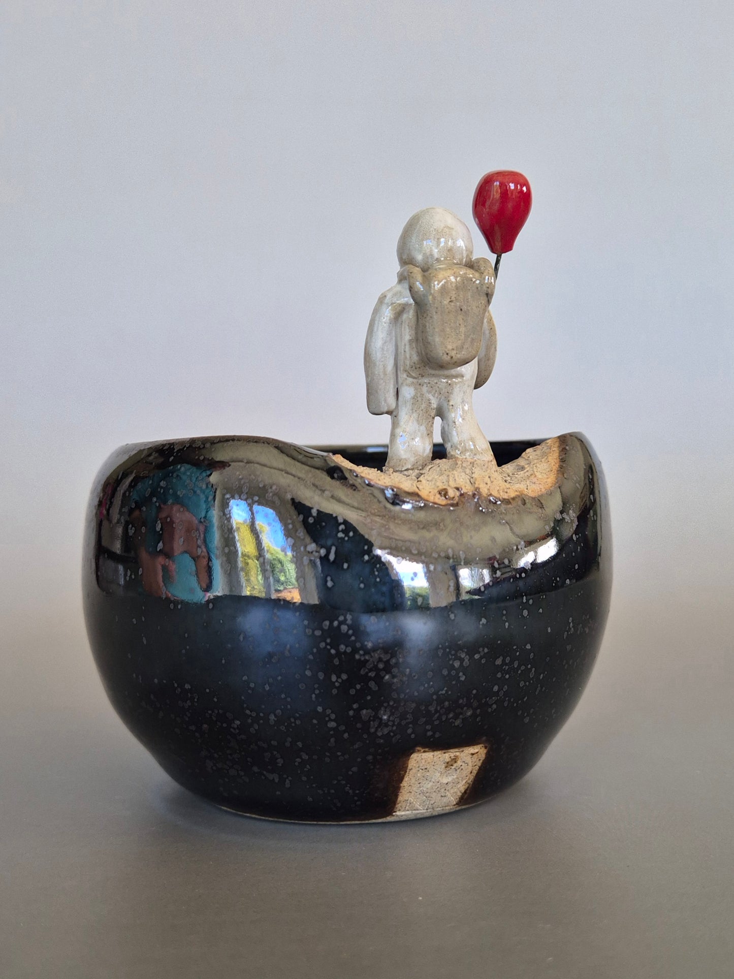 Ceramic bowl with a small sculptured figurine of an astronaut holding a red balloon. On a plain background
