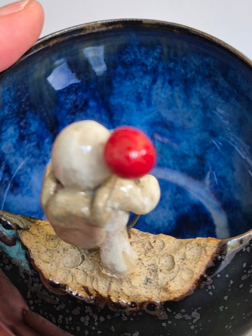 Ceramic bowl with a small sculptured figurine of an astronaut holding a red balloon. On a plain background