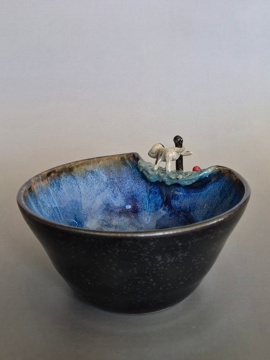 Ceramic bowl with small dog sculpture on the rim. On a plain background