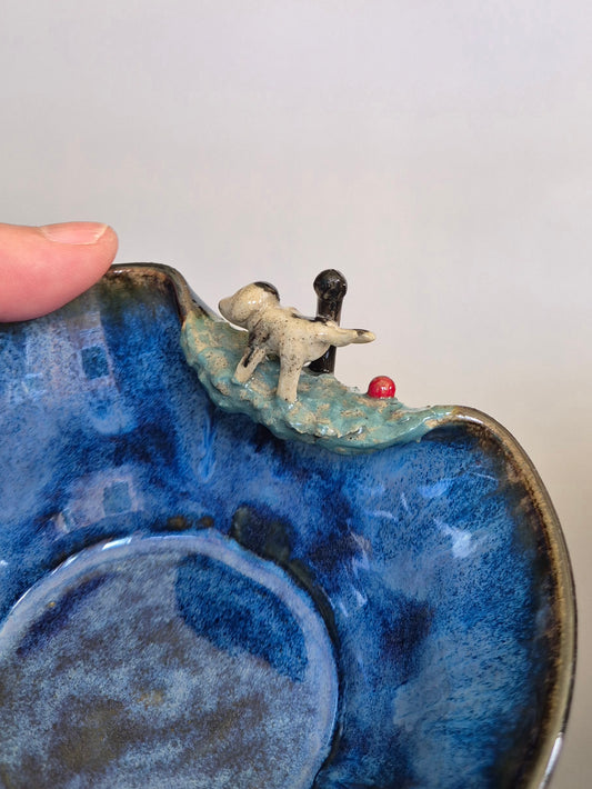Ceramic bowl with a blue glaze featuring small dog sculpture on a plain background