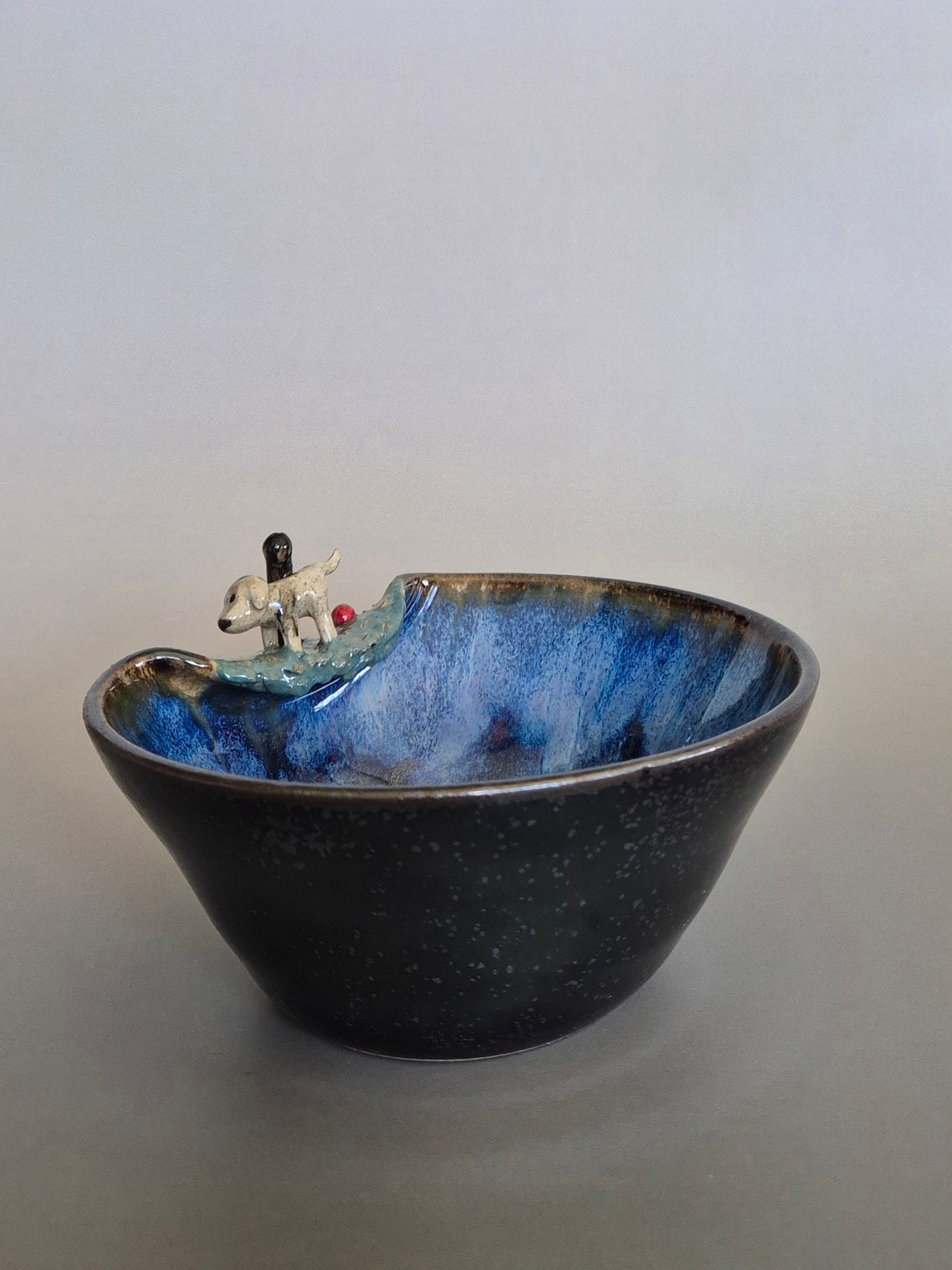 Ceramic bowl with blue interior and black exterior, featuring a small decorative scene on a plain background