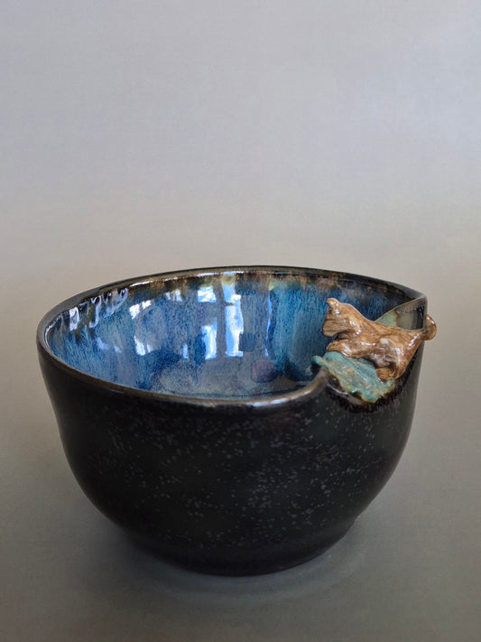 Ceramic bowl with blue interior and sculpted dog figurine on a gray background