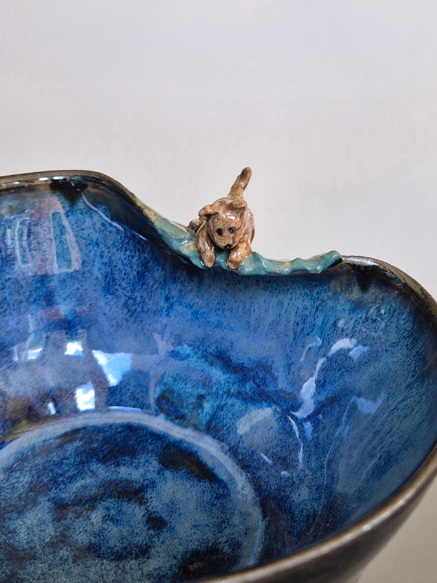 Blue ceramic bowl with a small dog figurine on a white background