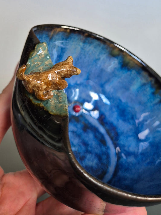 Ceramic bowl with blue glaze and a small dog figurine on a plain background