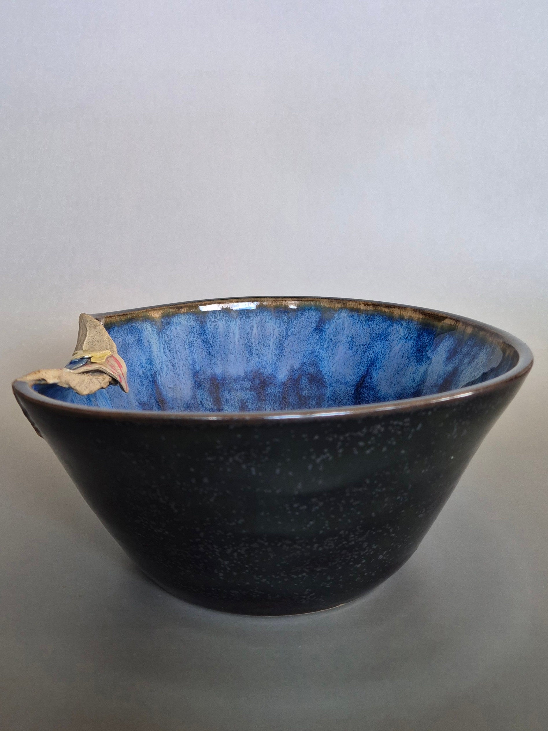 A ceramic bowl featuring sculptural details creating a miniature beach scene. On a plain background
