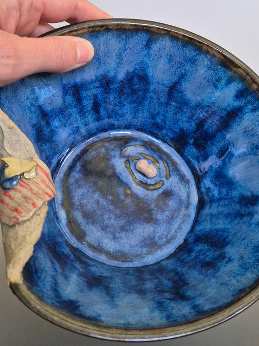 A ceramic bowl featuring sculptural details creating a miniature beach scene. On a plain background