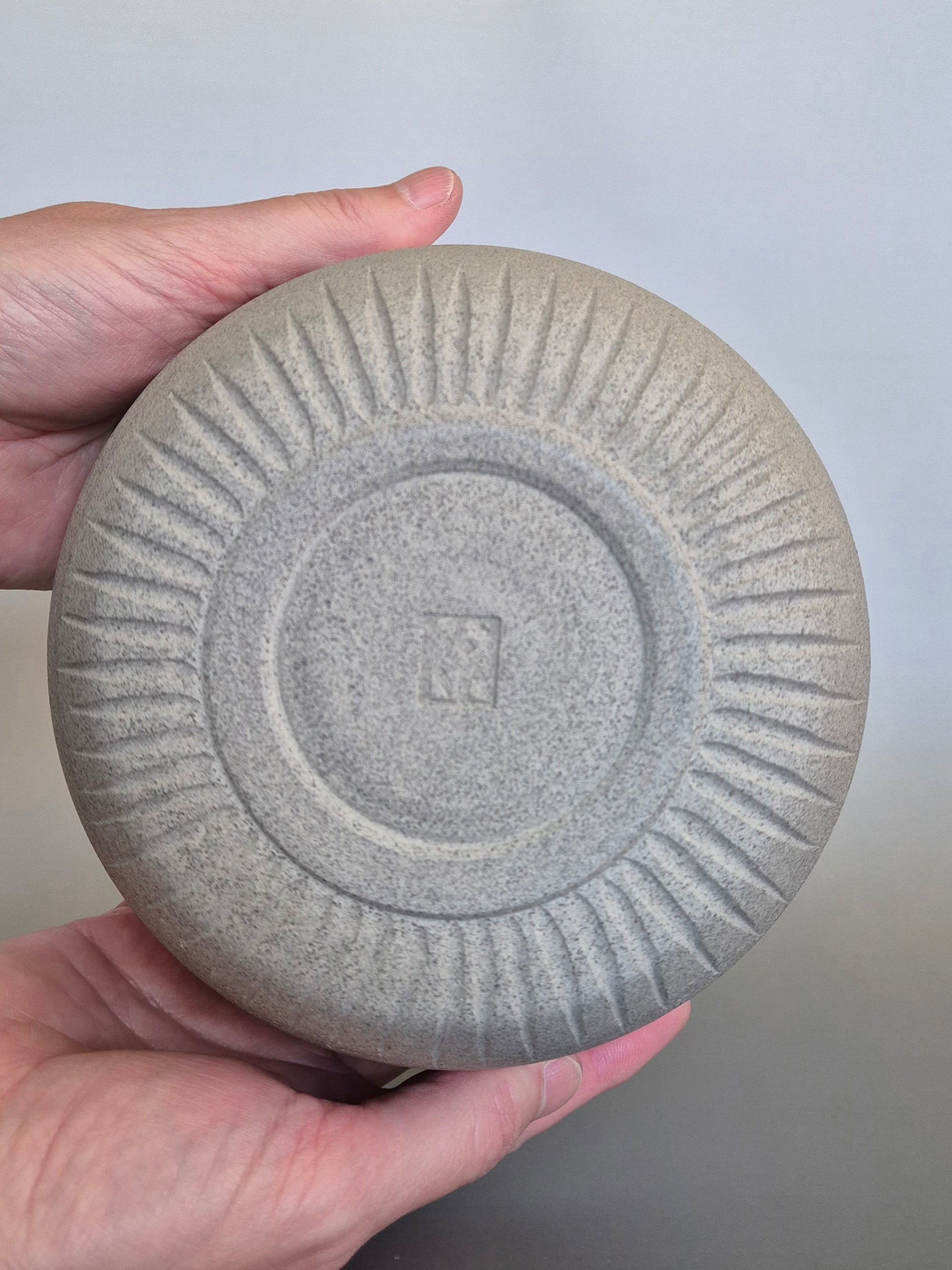 Hand holding a textured ceramic bowl to show the base, against a plain background