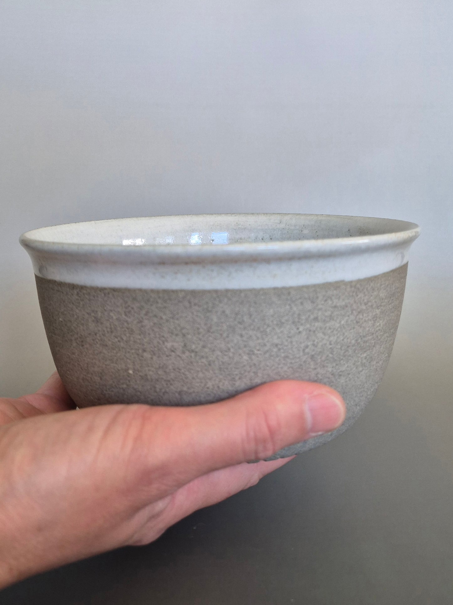 Hand holding a gray ceramic bowl against a plain background