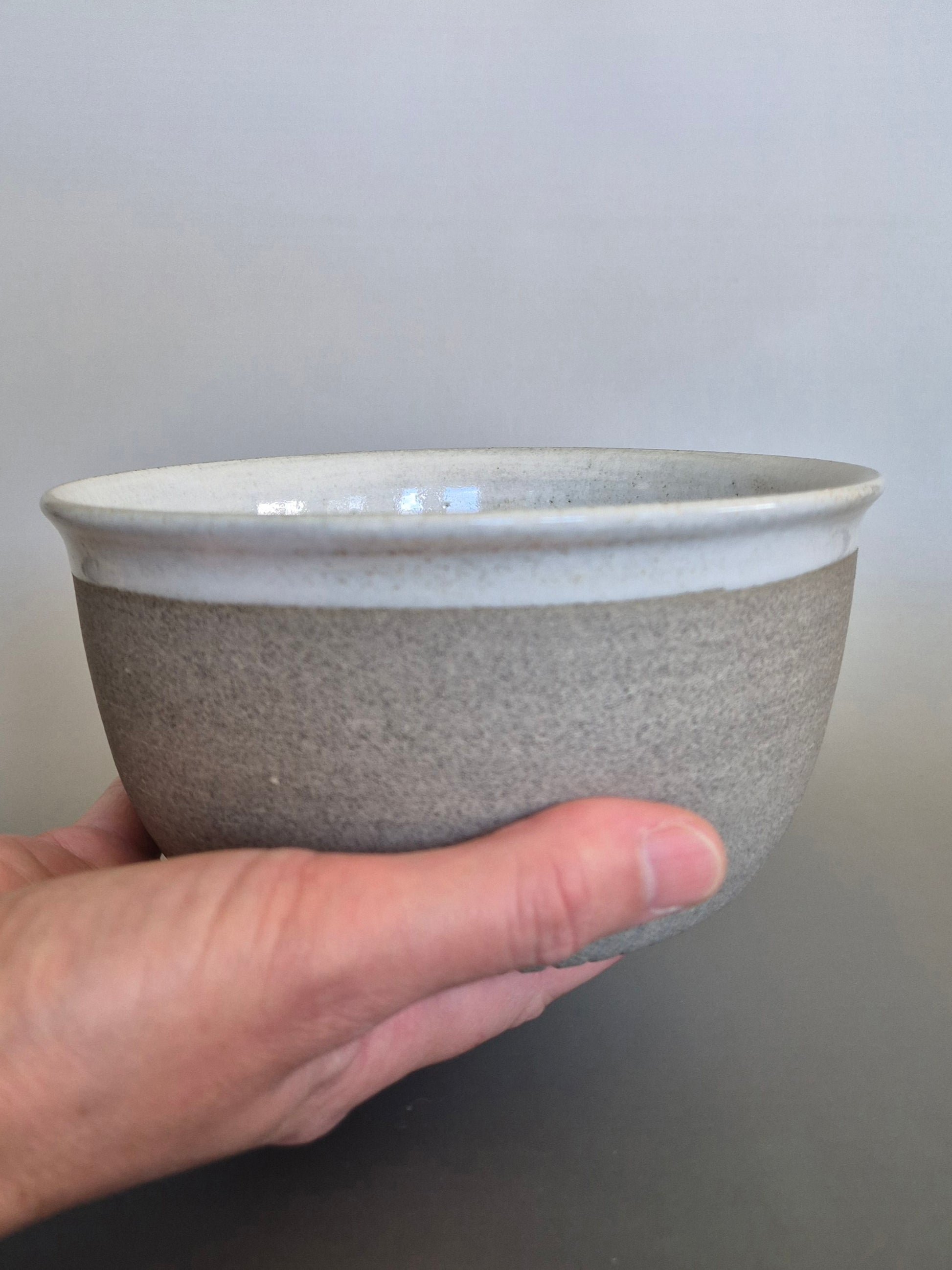 Hand holding a gray ceramic bowl against a plain background
