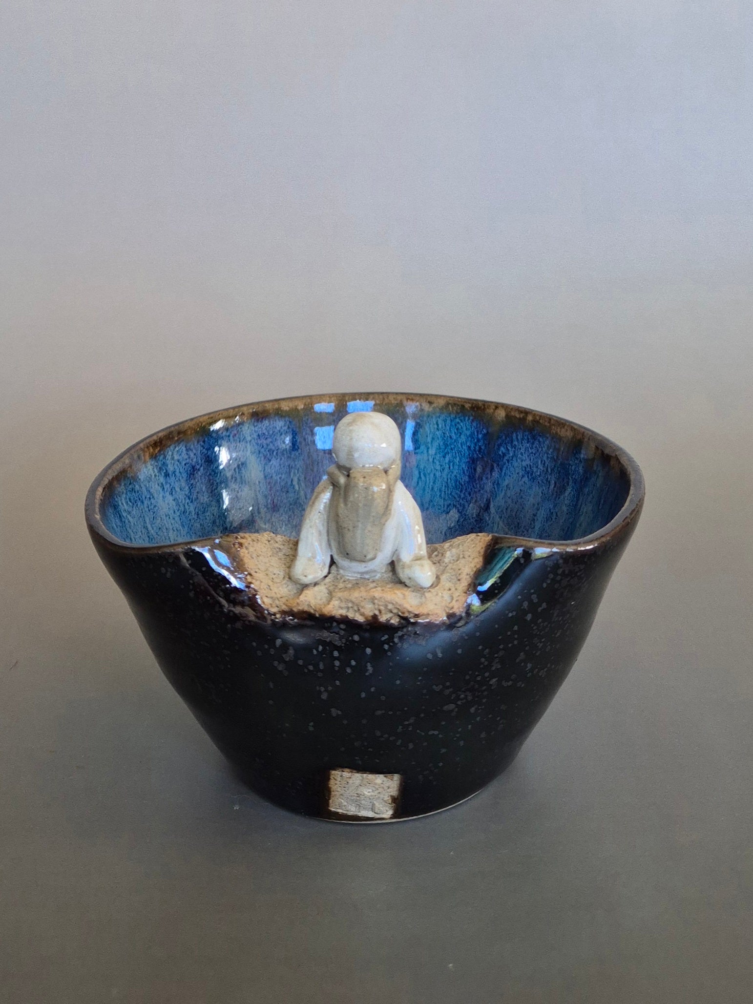 Small figurine of an astronaut sitting on the edge of a bowl. On a plain background