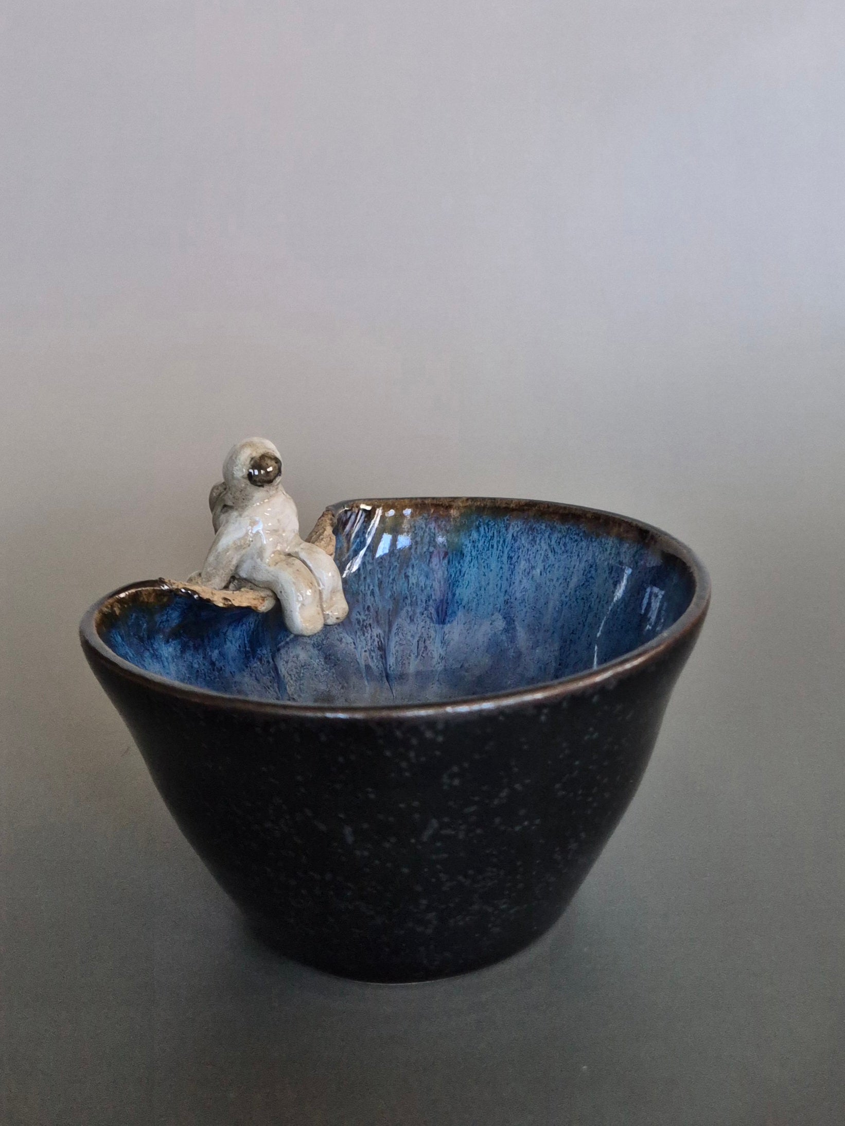 Small figurine of an astronaut sitting on the edge of a bowl. On a plain background