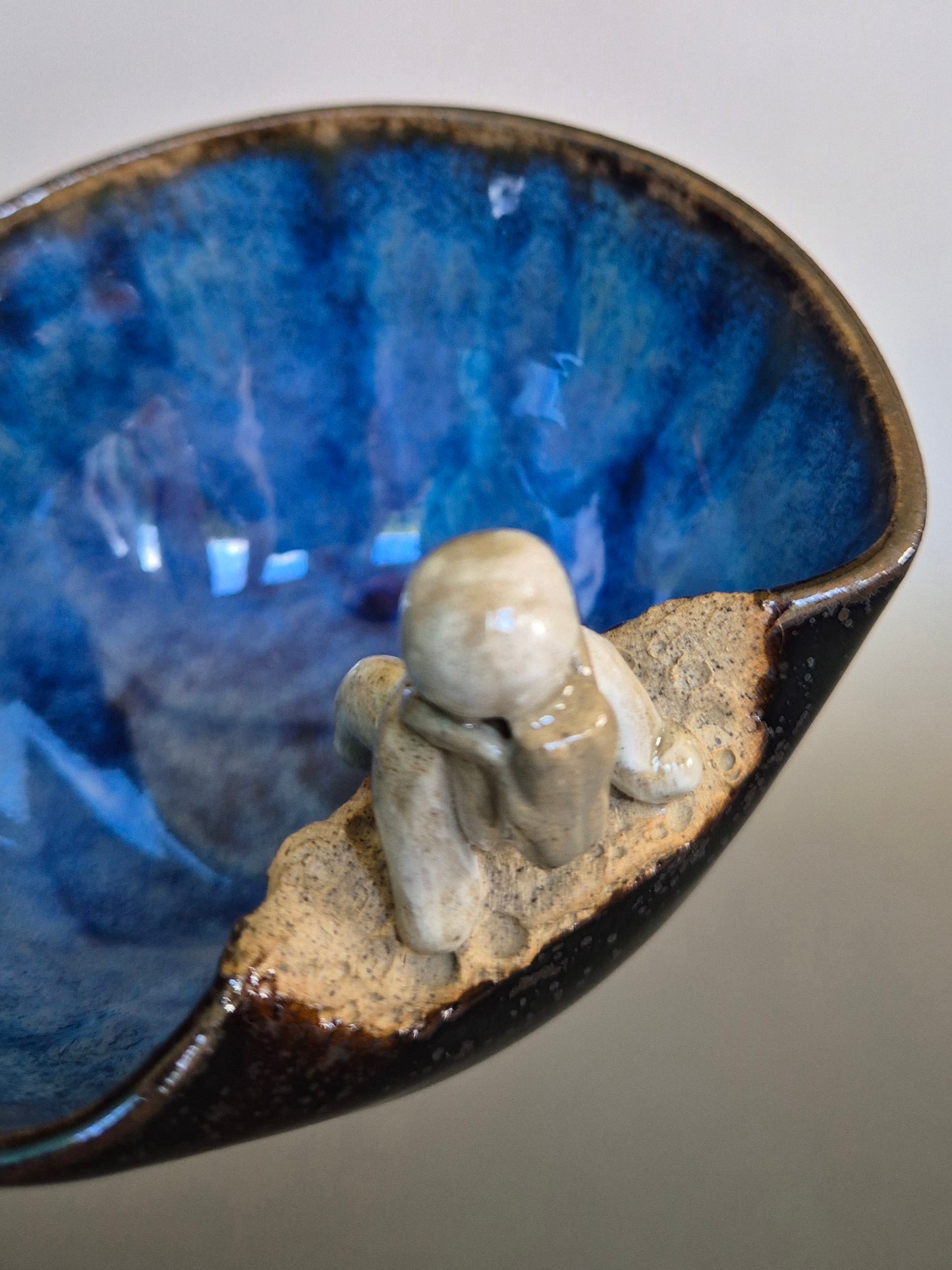 Close up of a small figurine of an astronaut sitting on the edge of a bowl. On a plain background