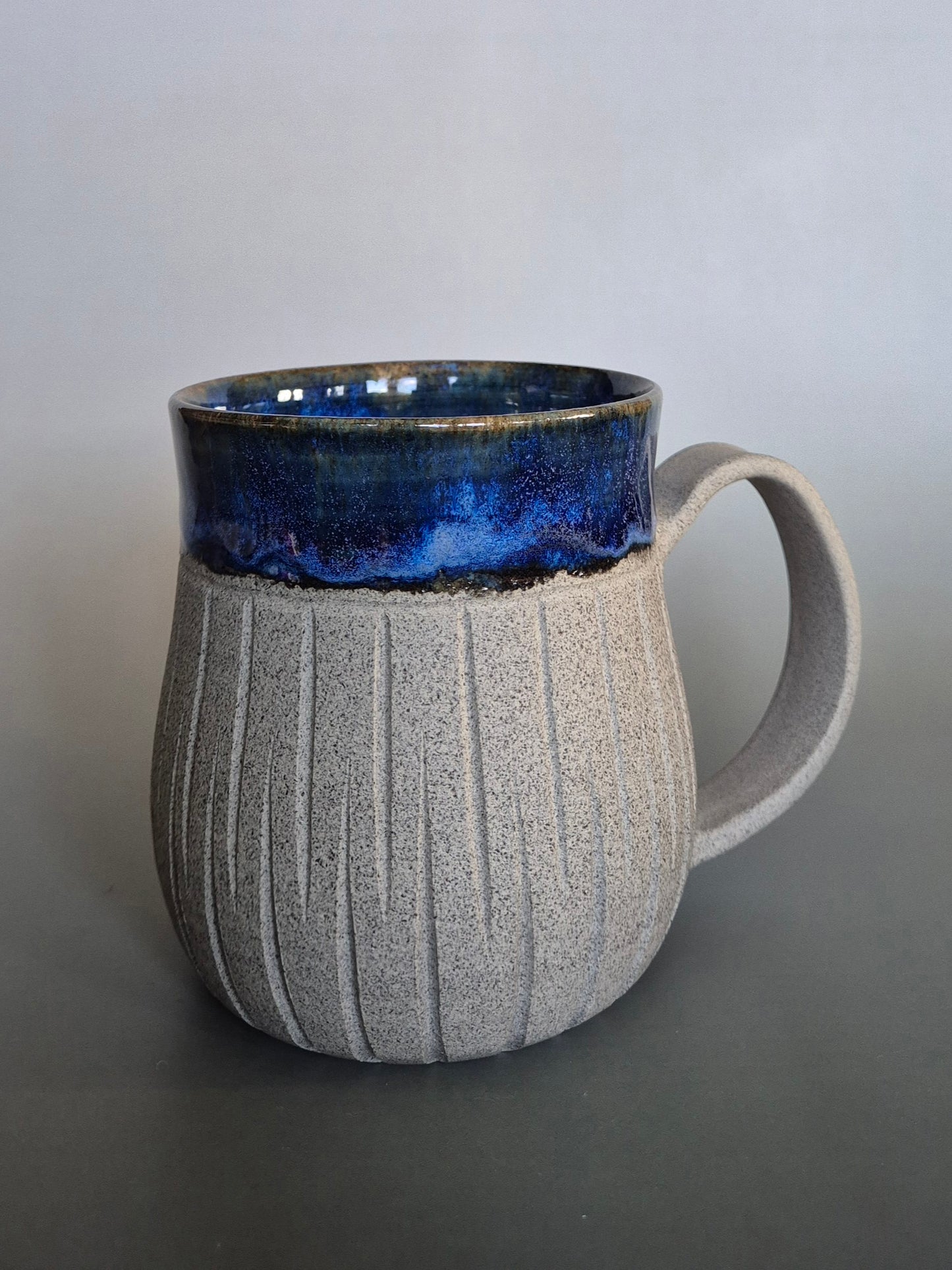 Ceramic mug with blue interior and textured gray exterior on a plain background