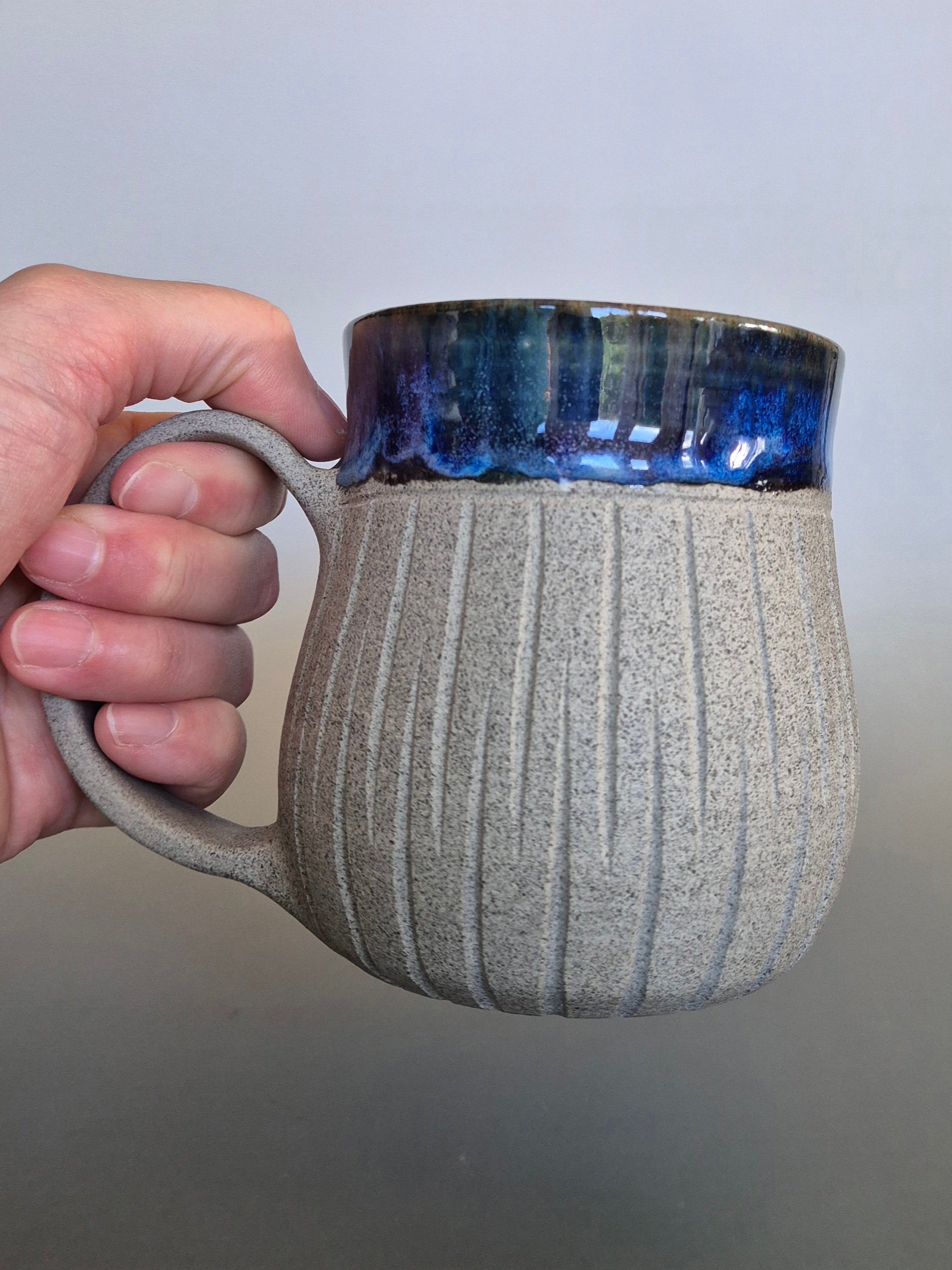 Hand holding a textured ceramic mug with a blue interior against a plain background