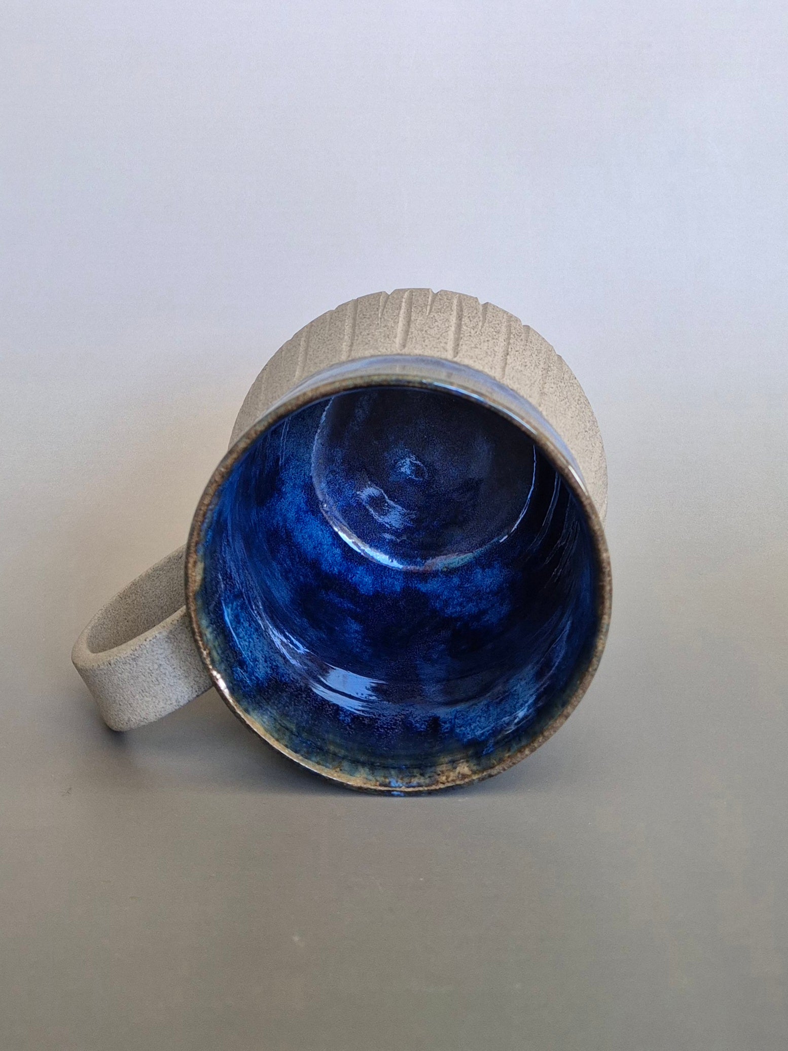 Ceramic mug with blue interior and grey exterior on a light gray background