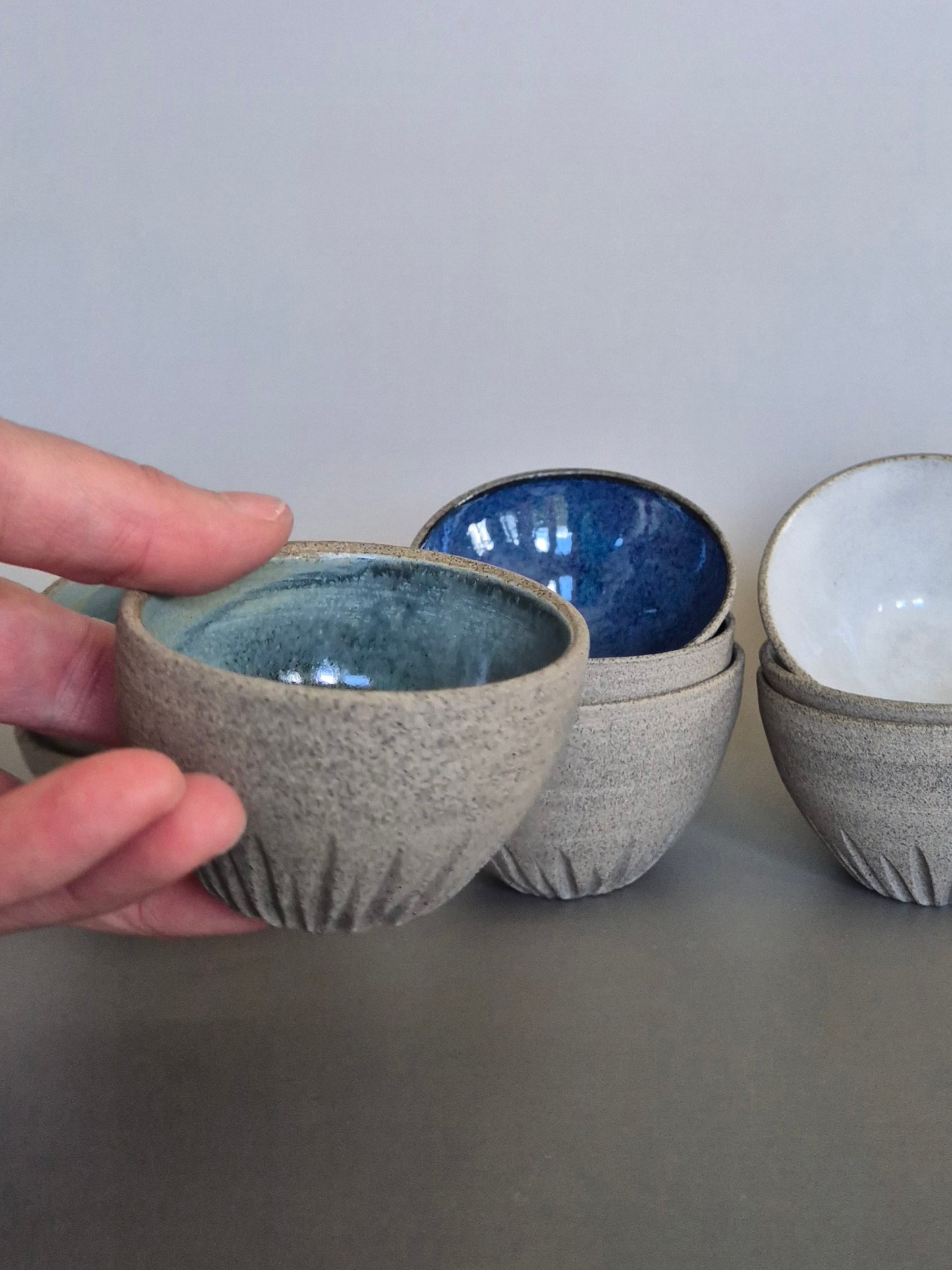 Hand holding a textured ceramic bowl with other bowls in the background on a gray surface.