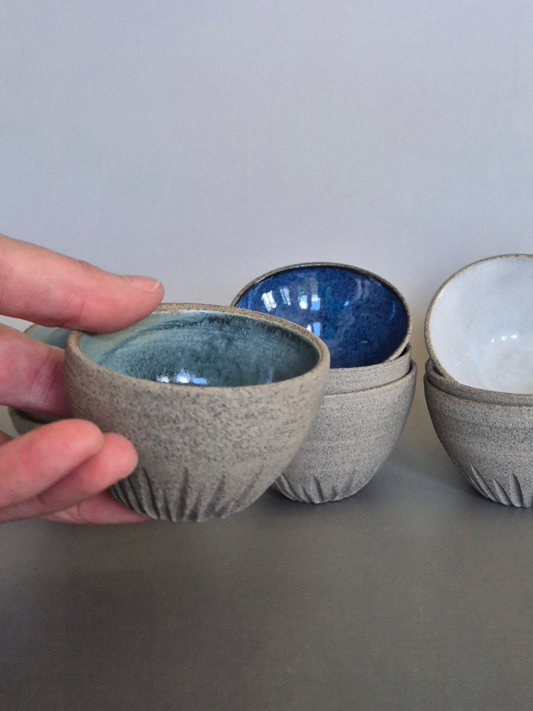 Hand holding a textured ceramic bowl with other bowls in the background on a gray surface.