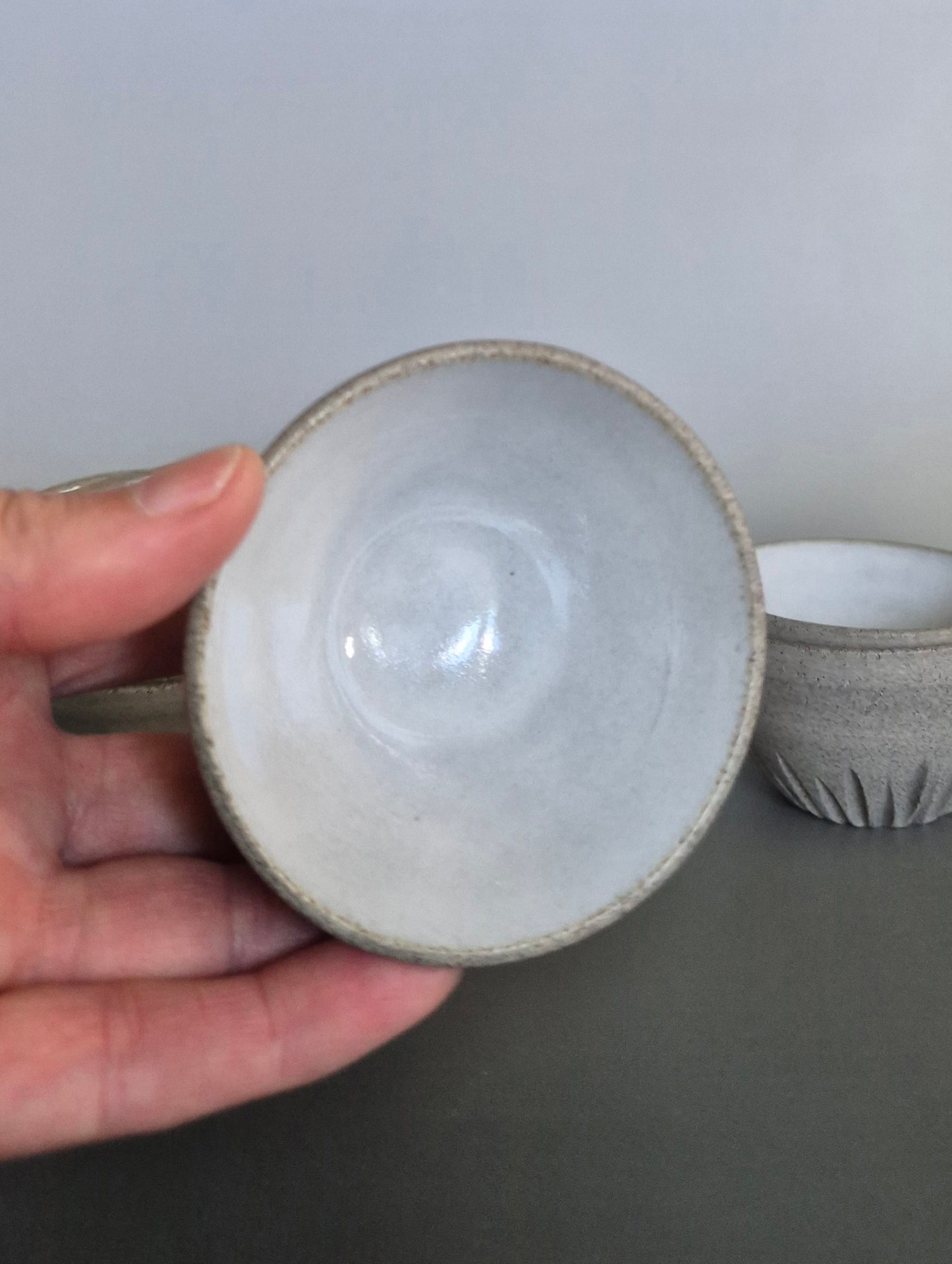 Ceramic cup held by a hand with a plain background