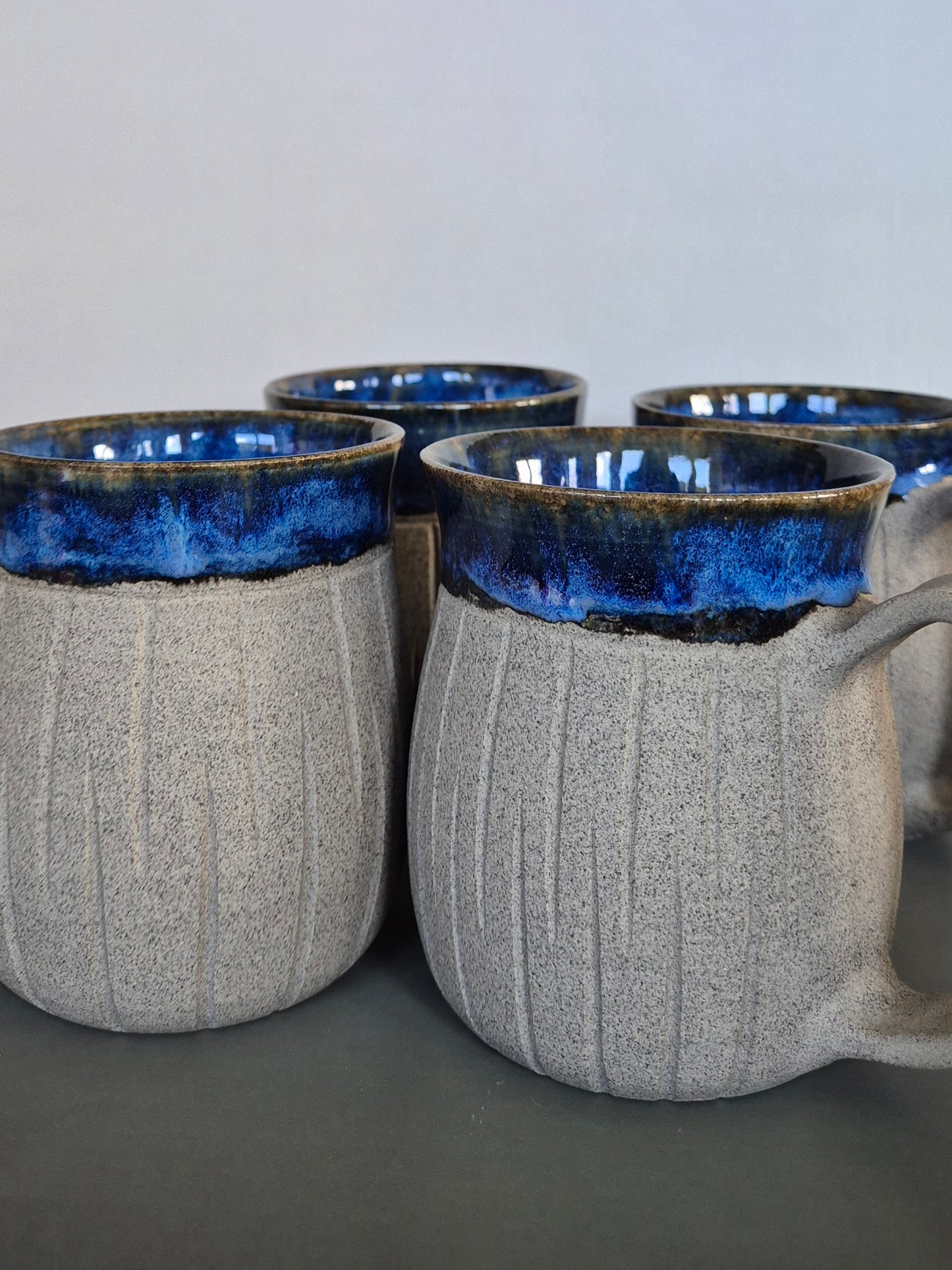 Set of four ceramic mugs with blue interior and gray exterior on a neutral background
