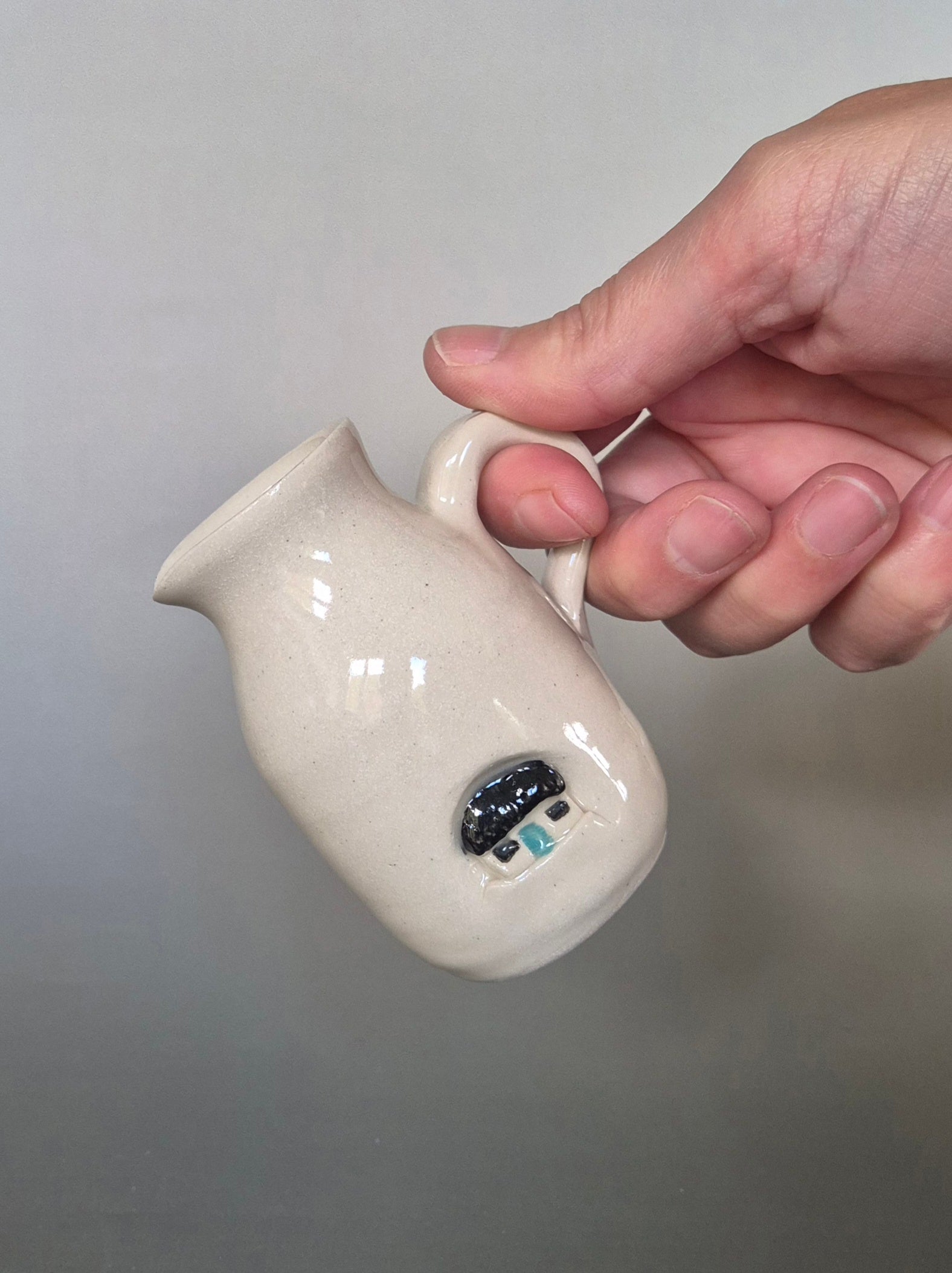 Hand holding a small white ceramic pitcher with a gray background