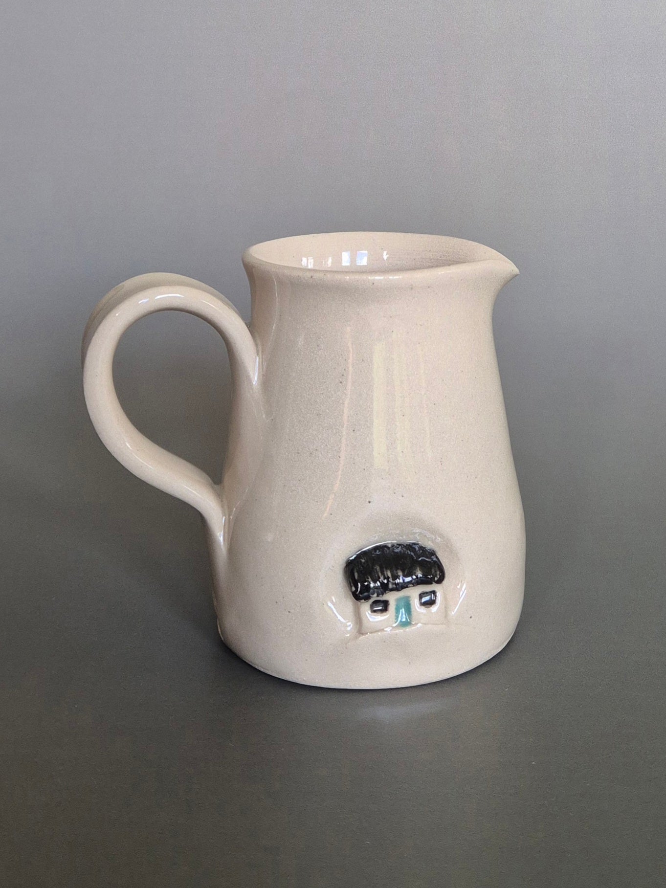 White ceramic pitcher with decorative elements on a gray background