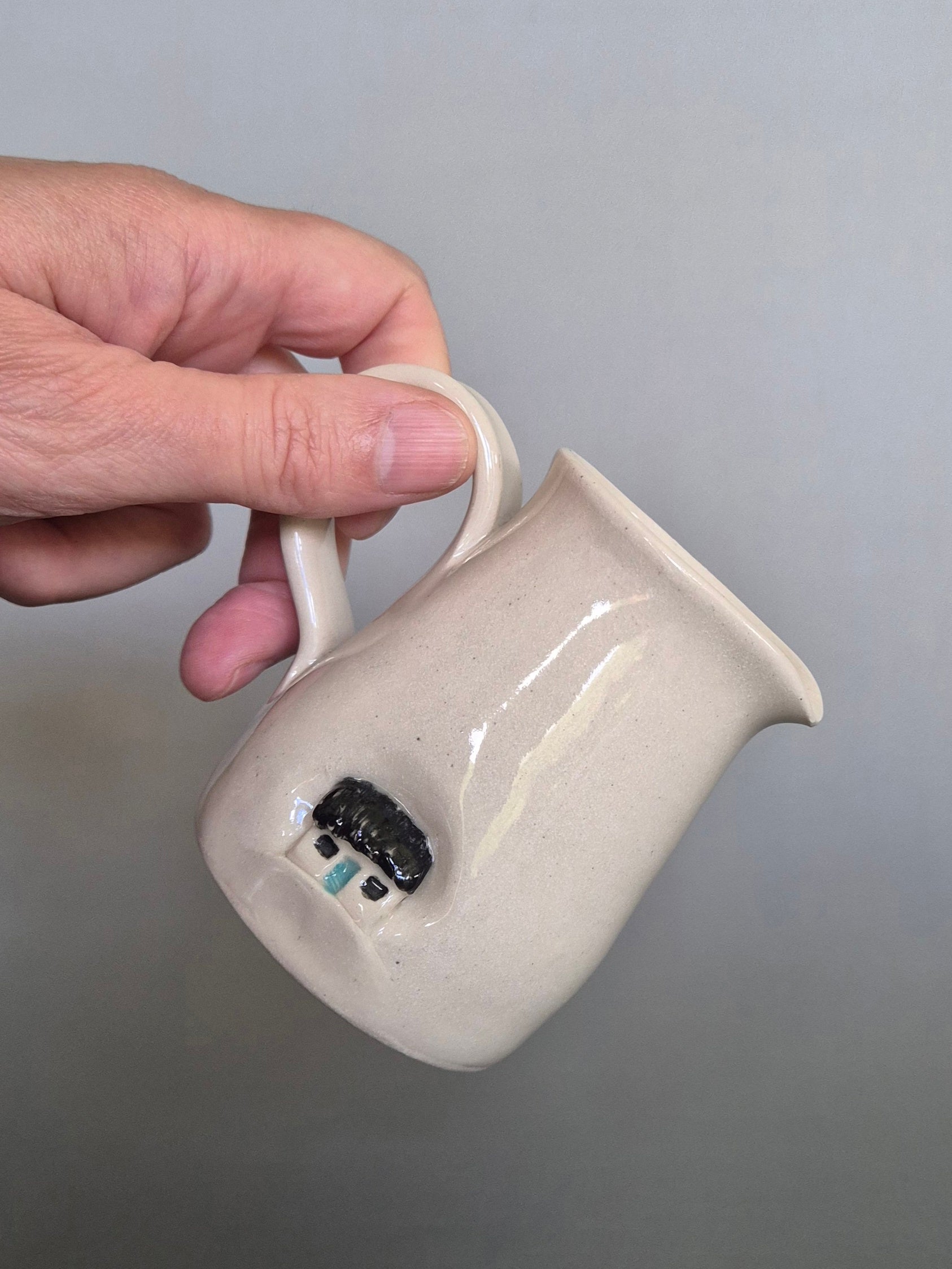 Hand holding a white ceramic pitcher with a gray background