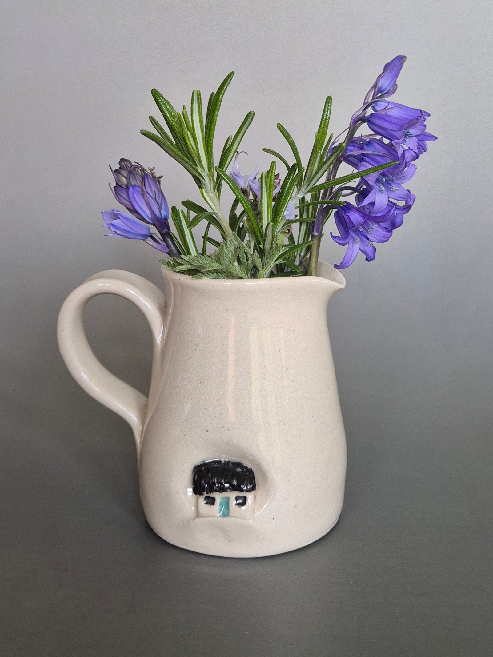 White ceramic pitcher with purple flowers on a gray background