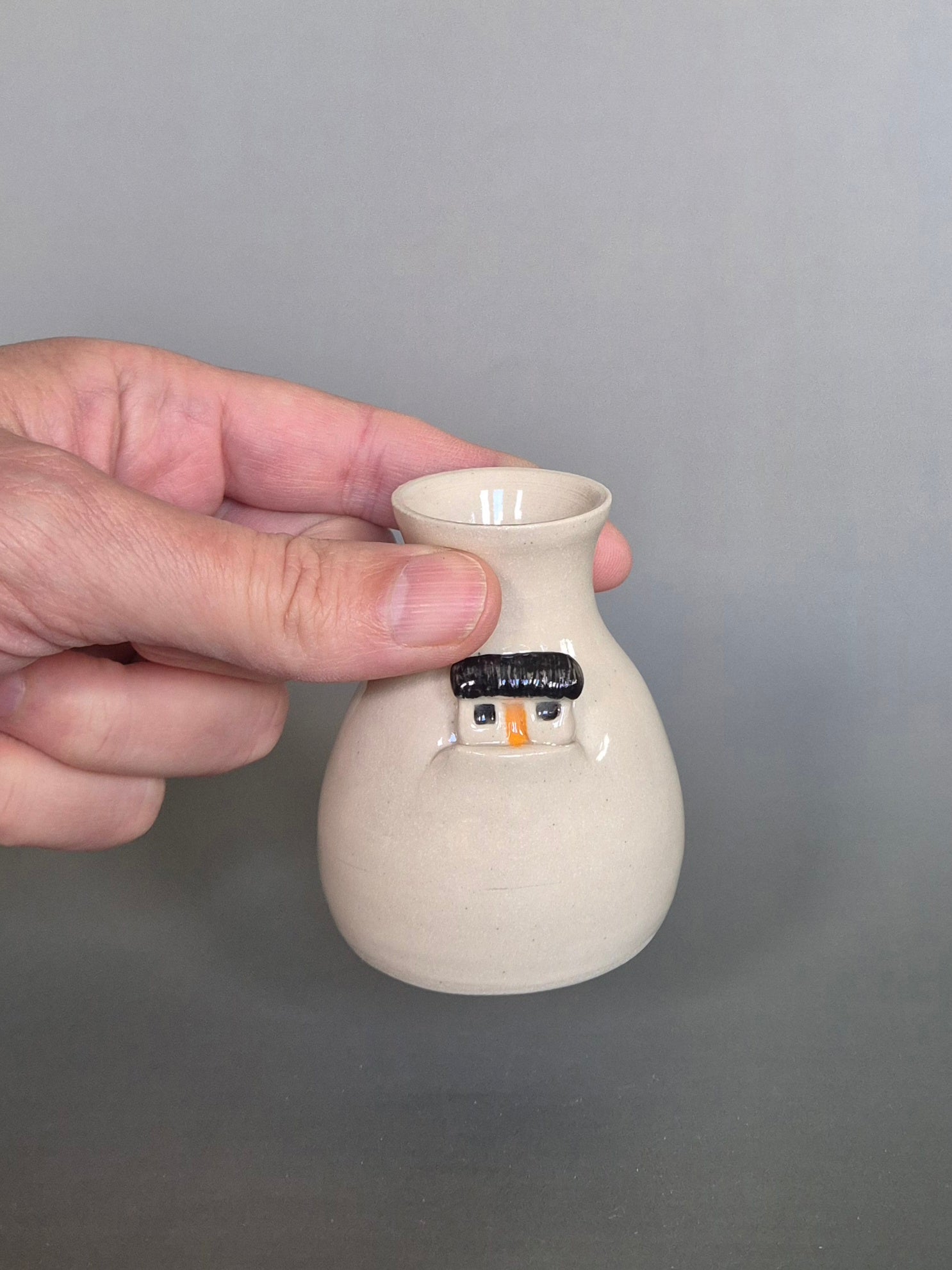 Hand holding a small white ceramic vase against a gray background