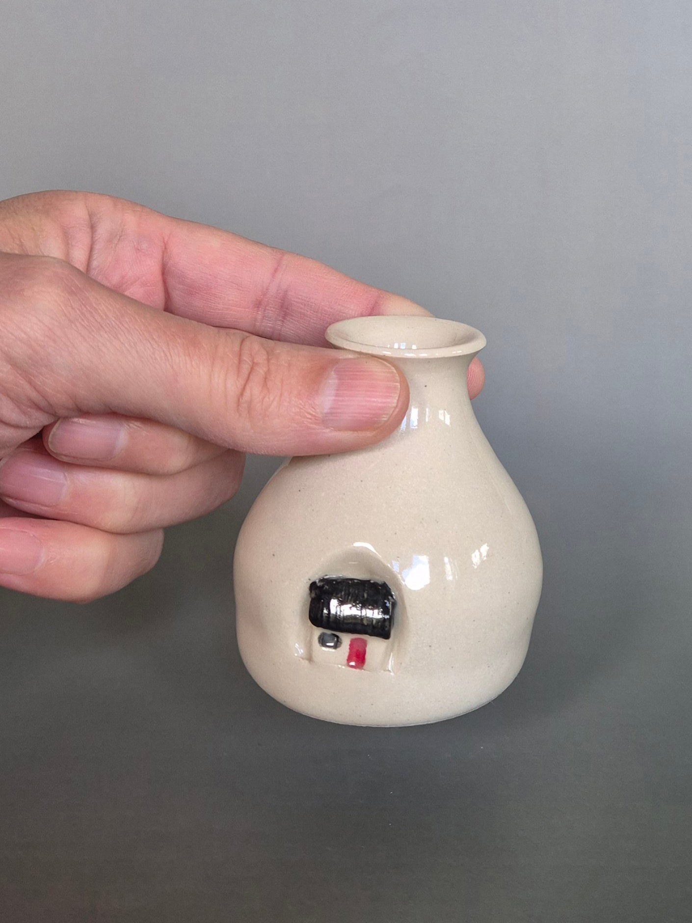A hand holding a small white ceramic bottle or bud vase. On a plain background
