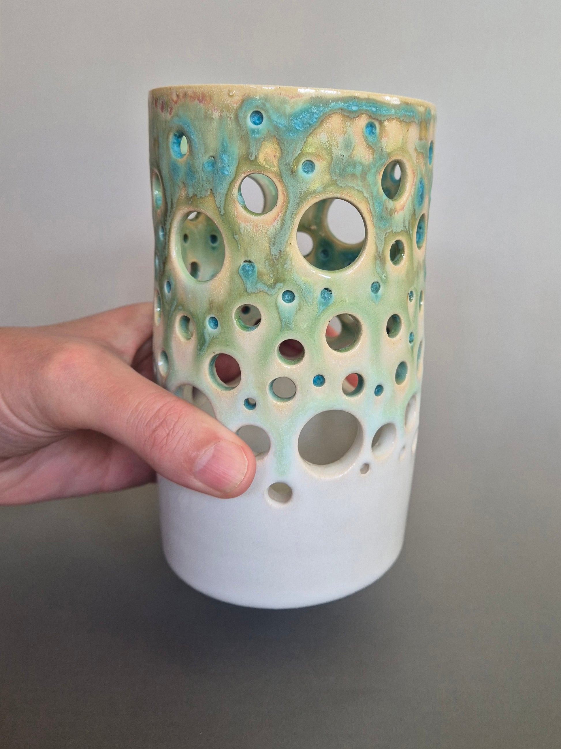 Ceramic vase with textured surface held by a hand against a neutral background