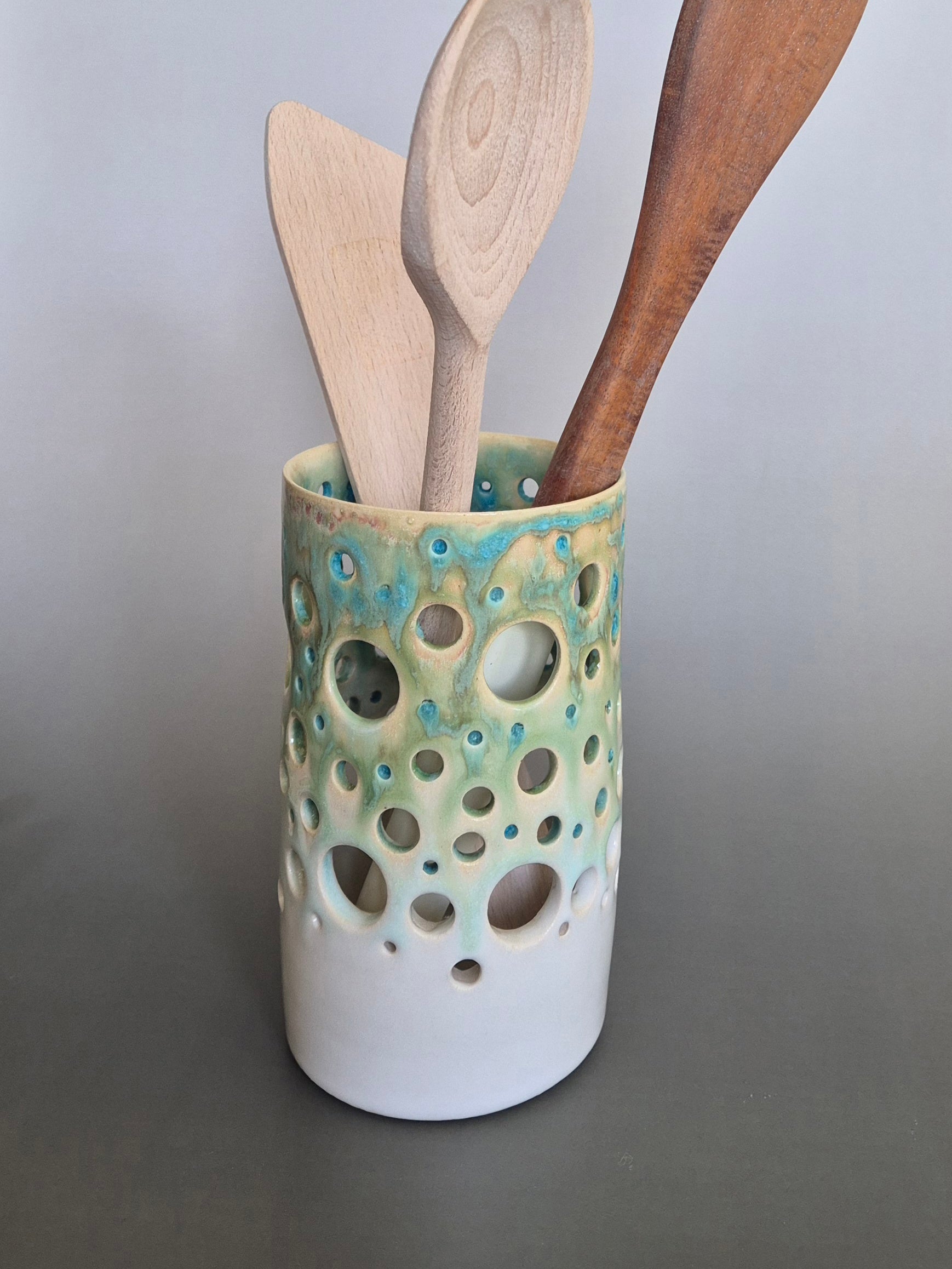 Ceramic utensil holder with wooden spoons on a gray background