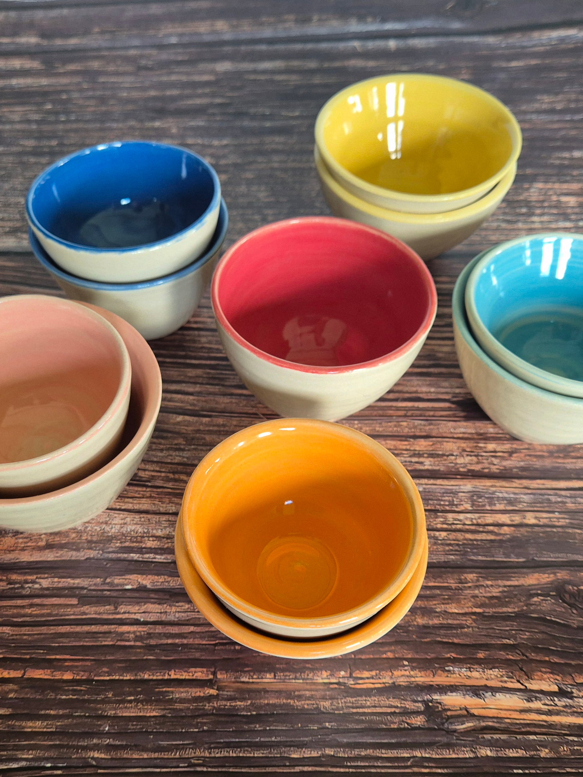 A collection of brightly coloured condiment or spice bowls. On a wooden table