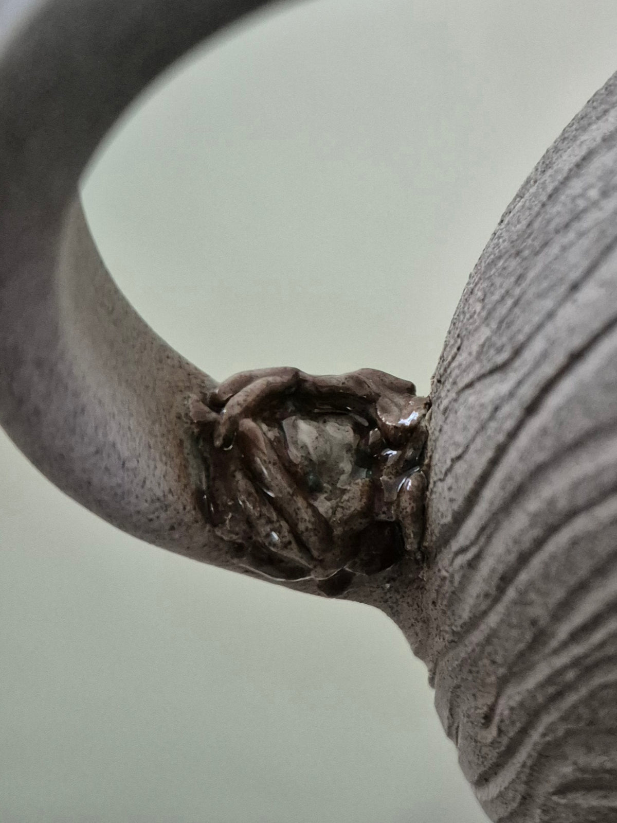 Close-up of a textured gray ceramic mug handle with a little birds nest and eggs, set against a soft, light gray background.