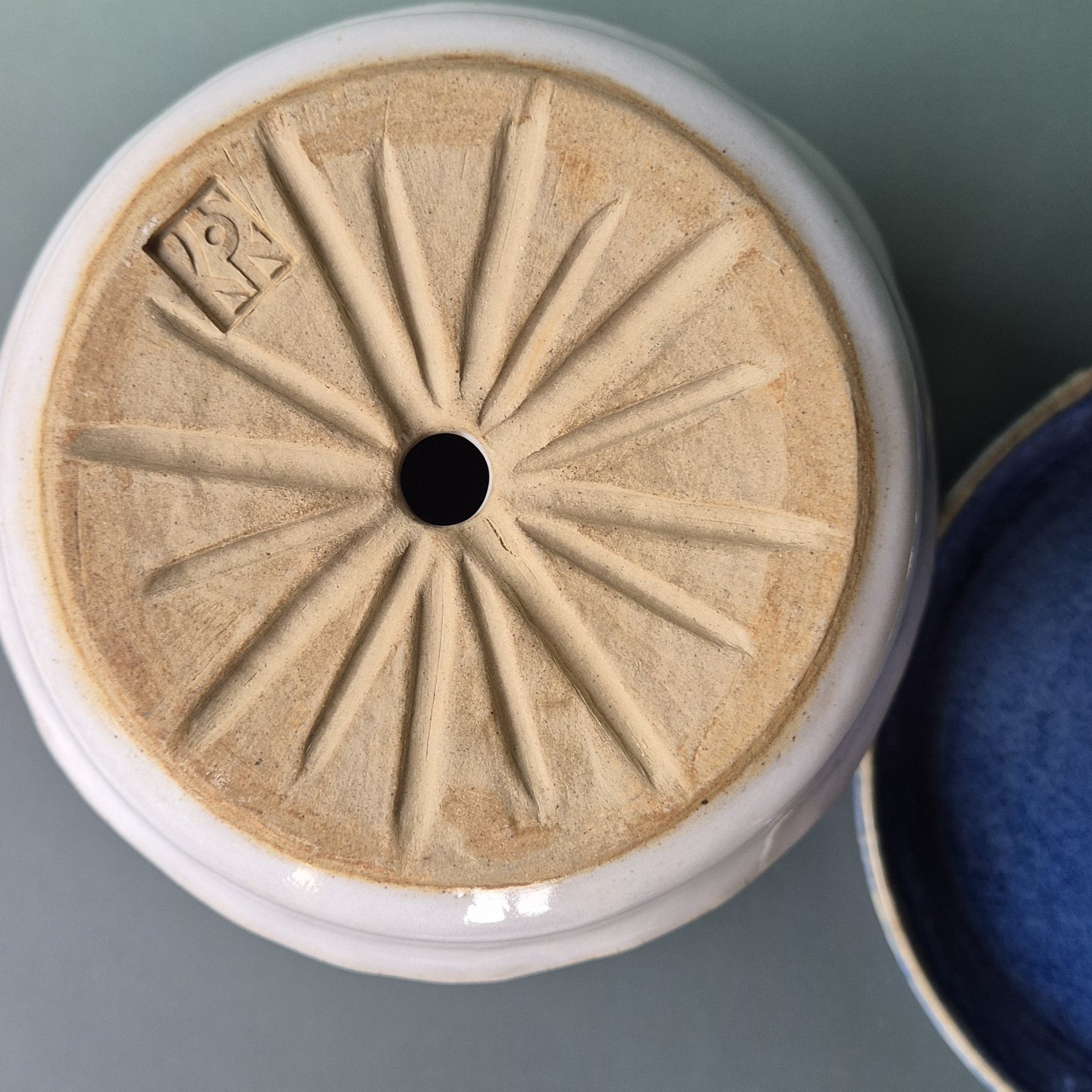 Close-up of a ceramic planter base with decorative patterns on a gray background, next to a blue glazed saucer