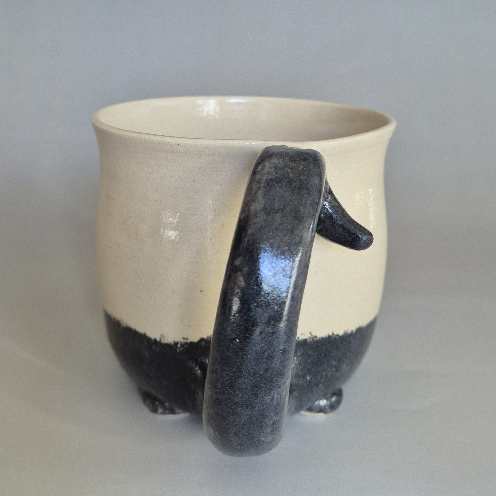 Ceramic cat mug with a black tail handle on a gray background