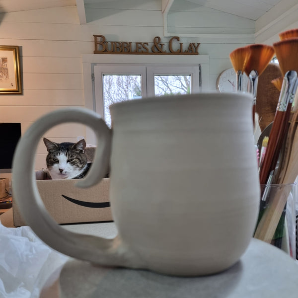 Cat peeking out from behind a clay mug with a snowy scene in the background