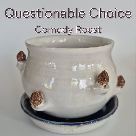 Ceramic planter with tiny hut sculptures on a white background, text 'Questionable Choice Comedy Roast' above.
