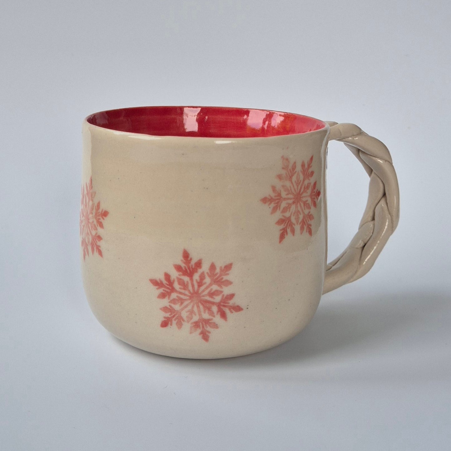 Beige mug with pink interior and snowflake patterns on a light gray background