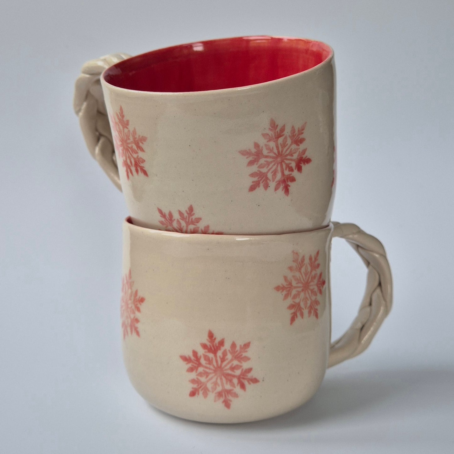 Two ceramic mugs with pink snowflake patterns on a light gray background