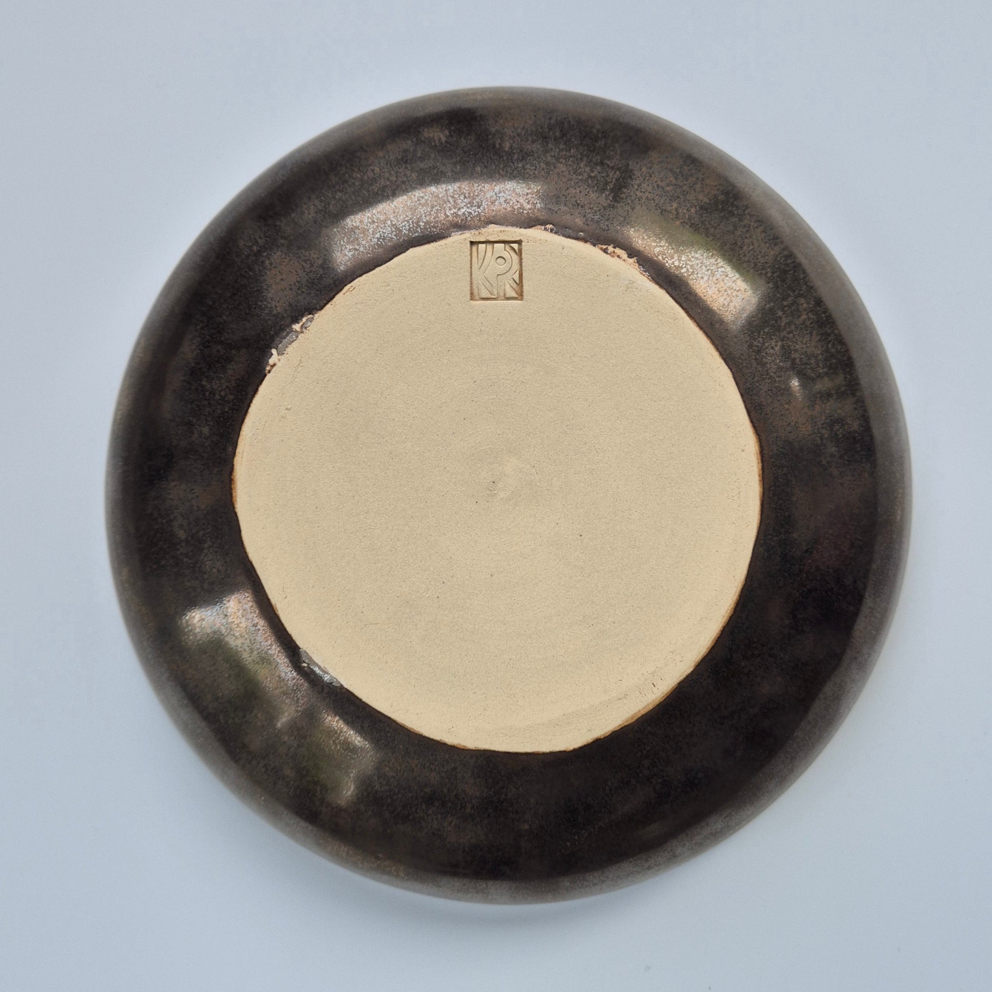Base of a round ceramic platter with a dark bronze glaze on a light gray background