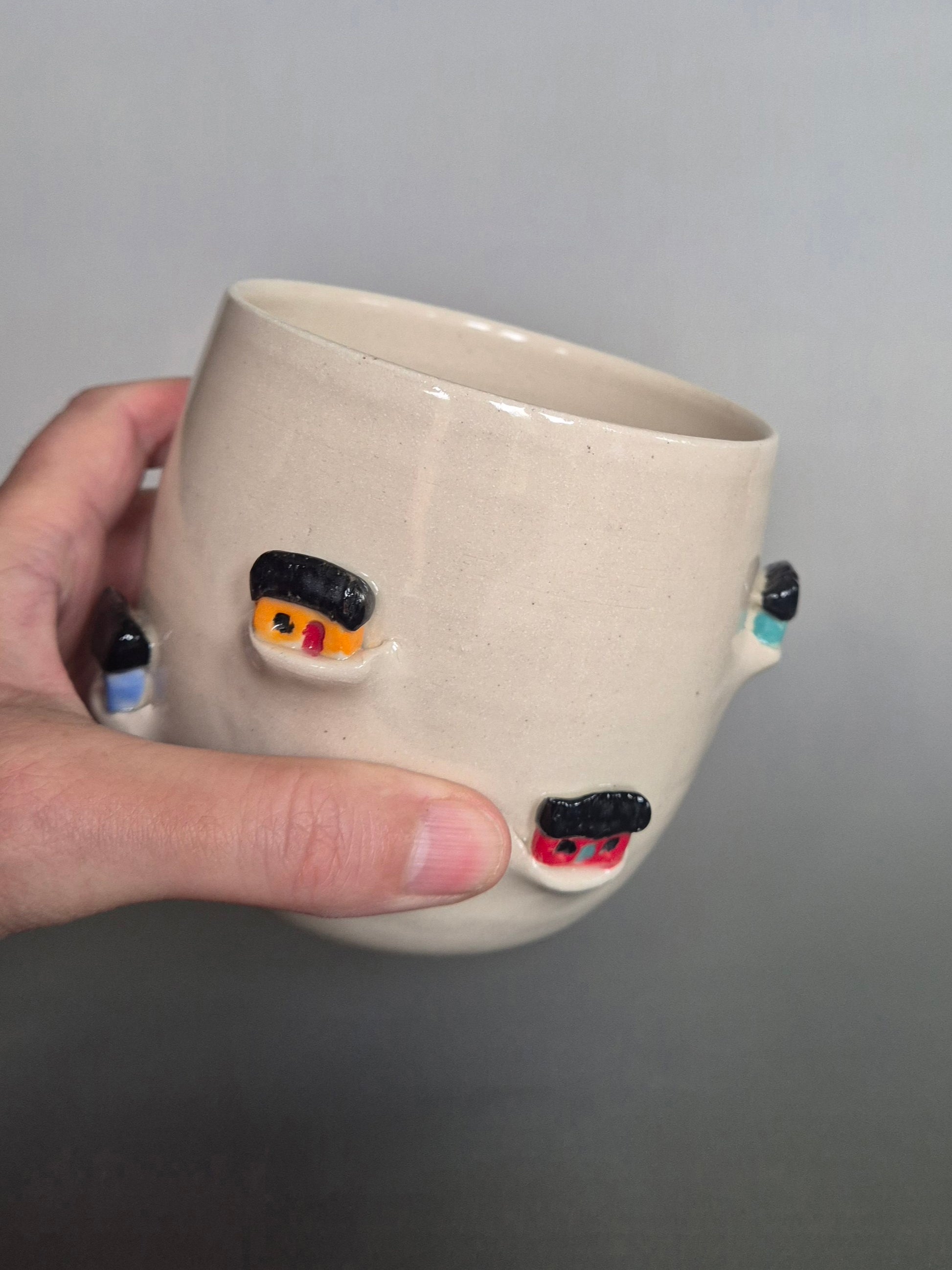 Hand holding a Ceramic pot with tiny sculptural houses on a gray background