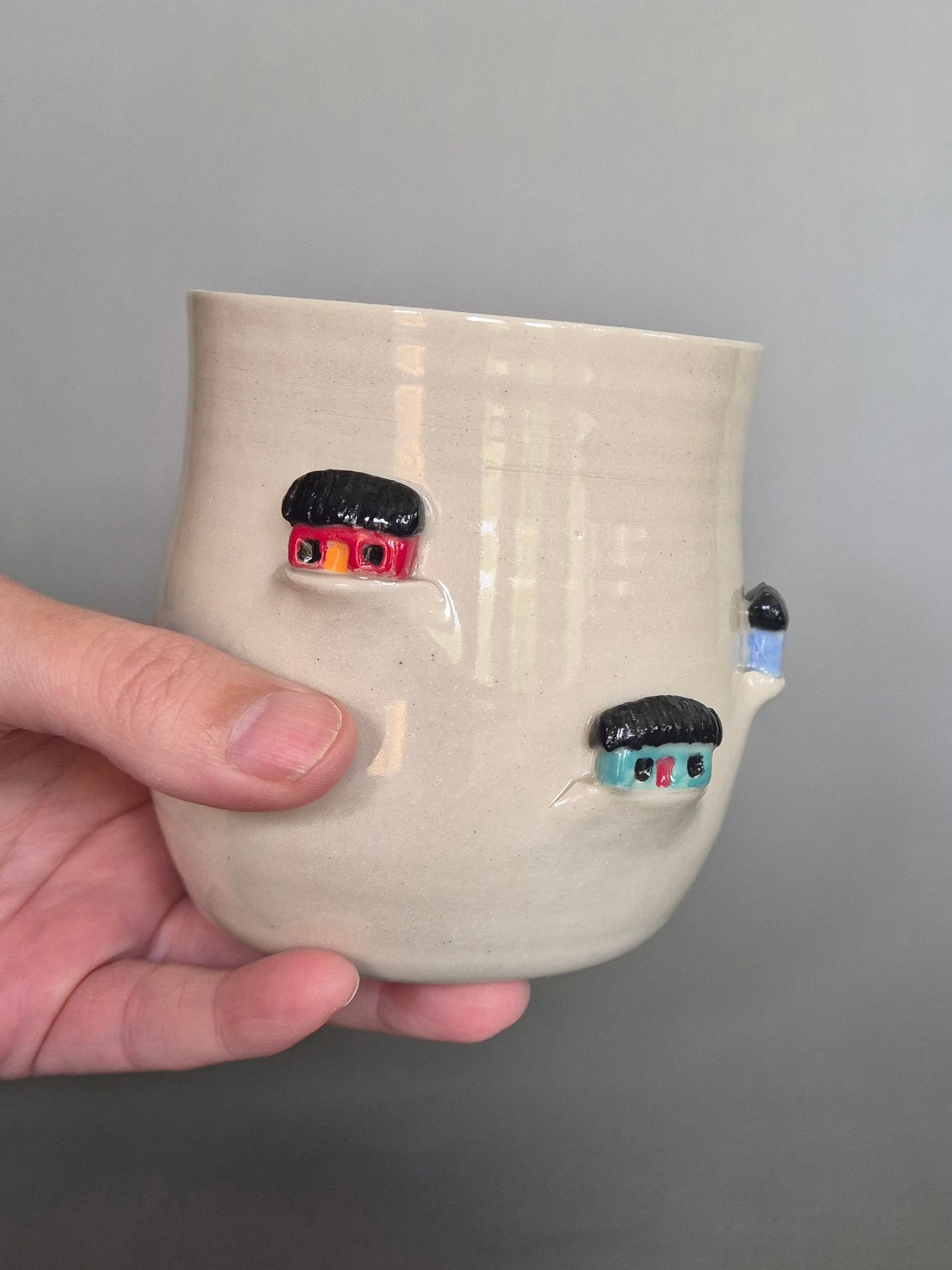 Hand holding a ceramic pot with decorative elements on a gray background